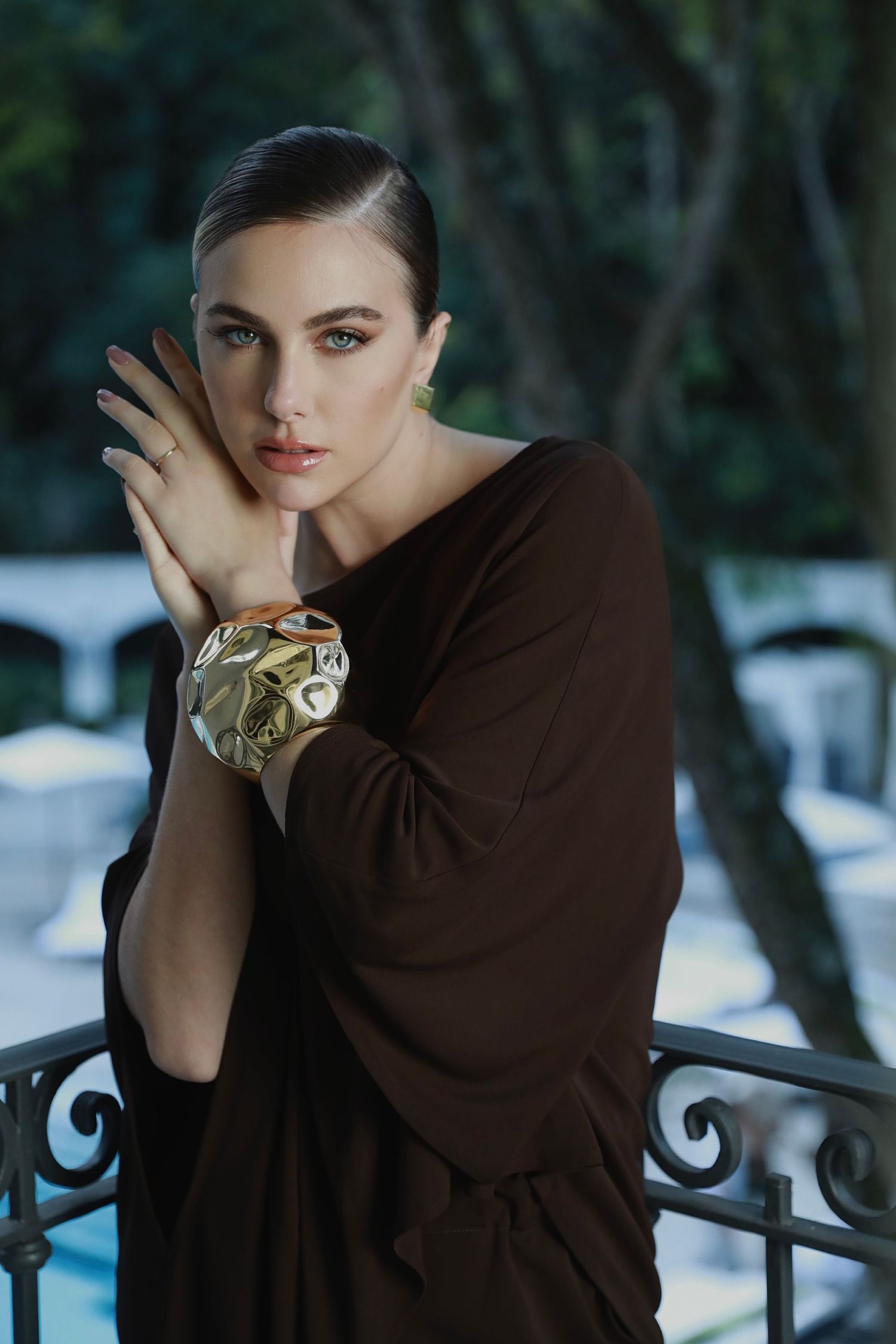 An elegant portrait of someone in a brown dress posing with a decorative gold bracelet.