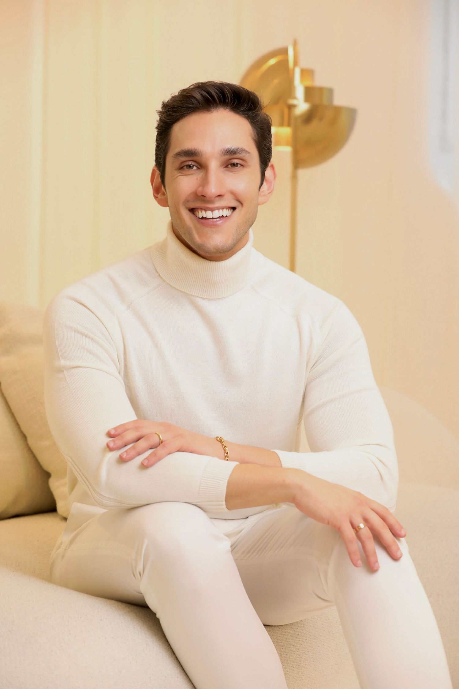 Professional portrait of man in cream turtleneck sweater sitting on beige couch.