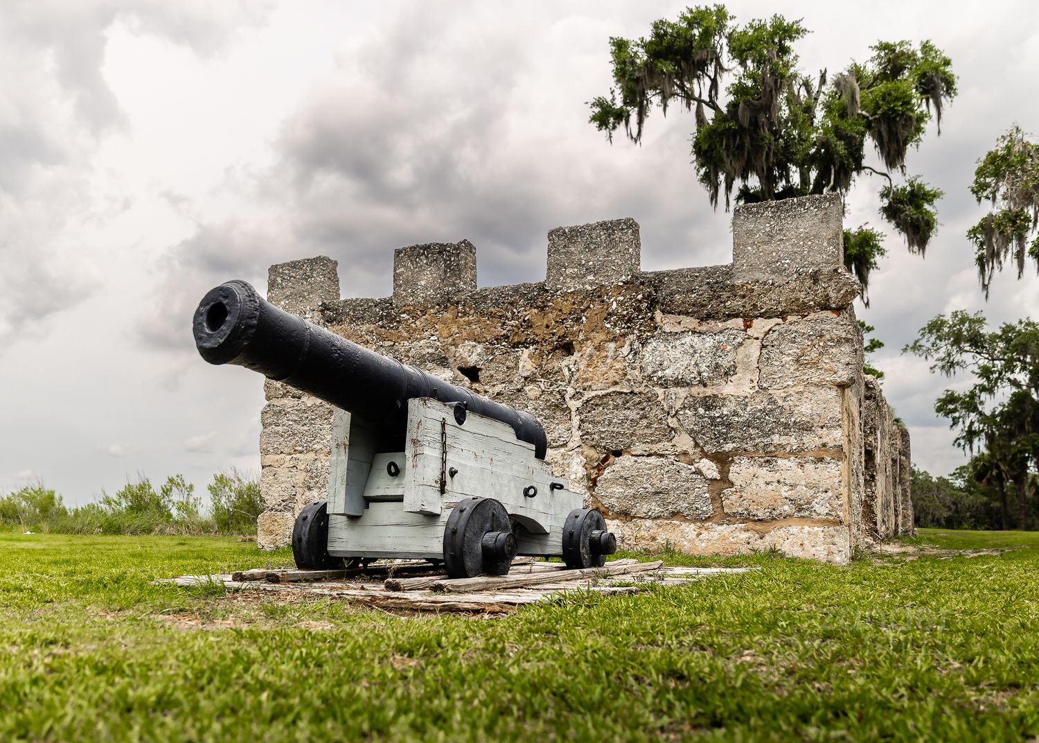 A photograph of a canon in front of an old fort on a grass field