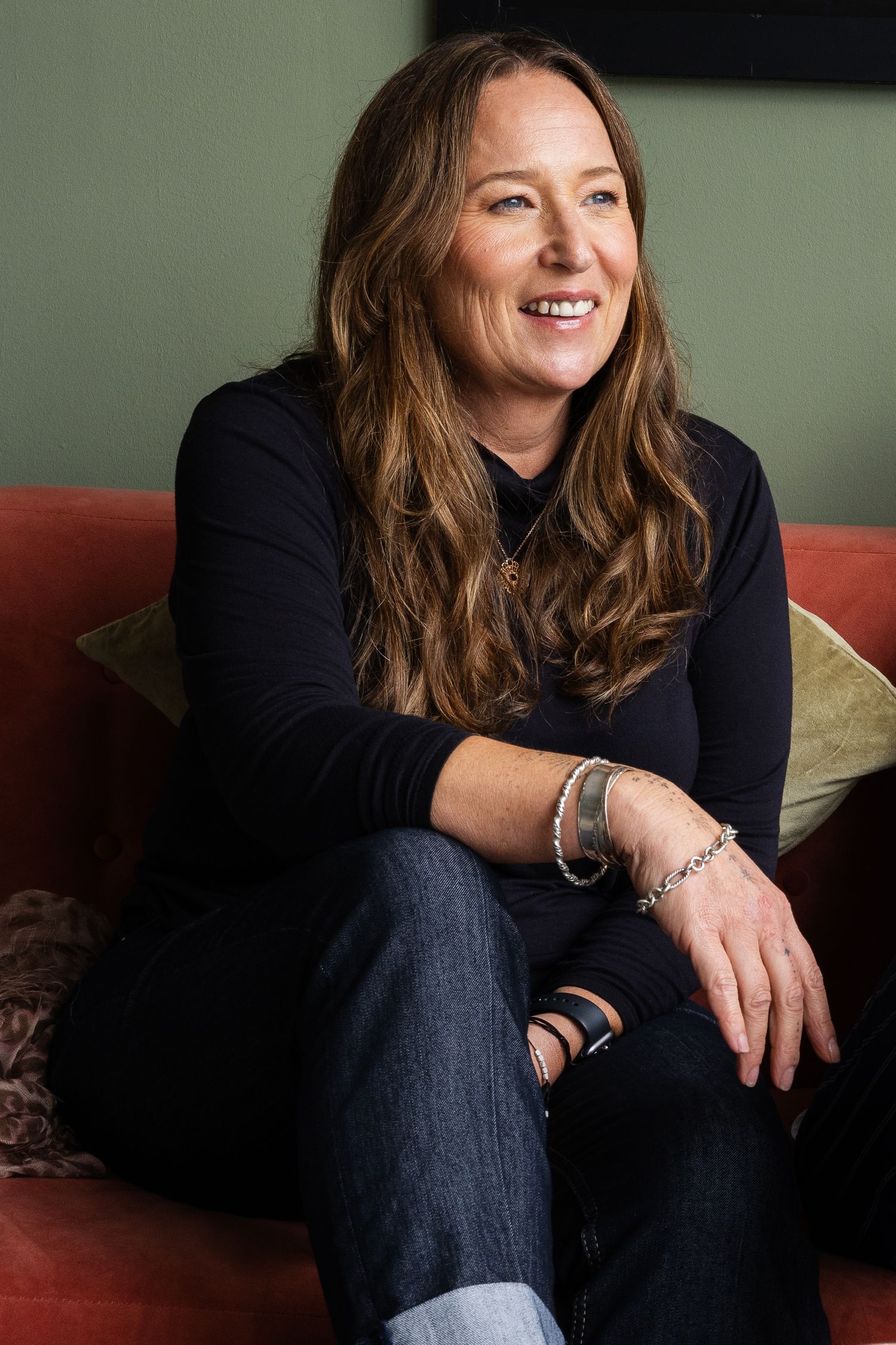 a portrait of a white woman with her arm leaning on her leg smiling and looking to the right