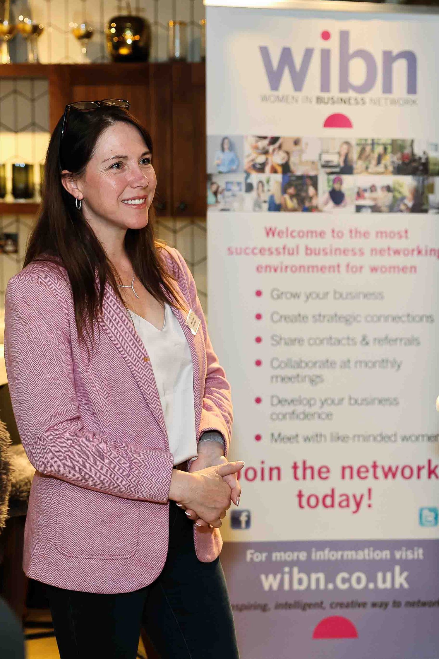 Women in pink jacket next to a pop up banner featuring Women in Business Network