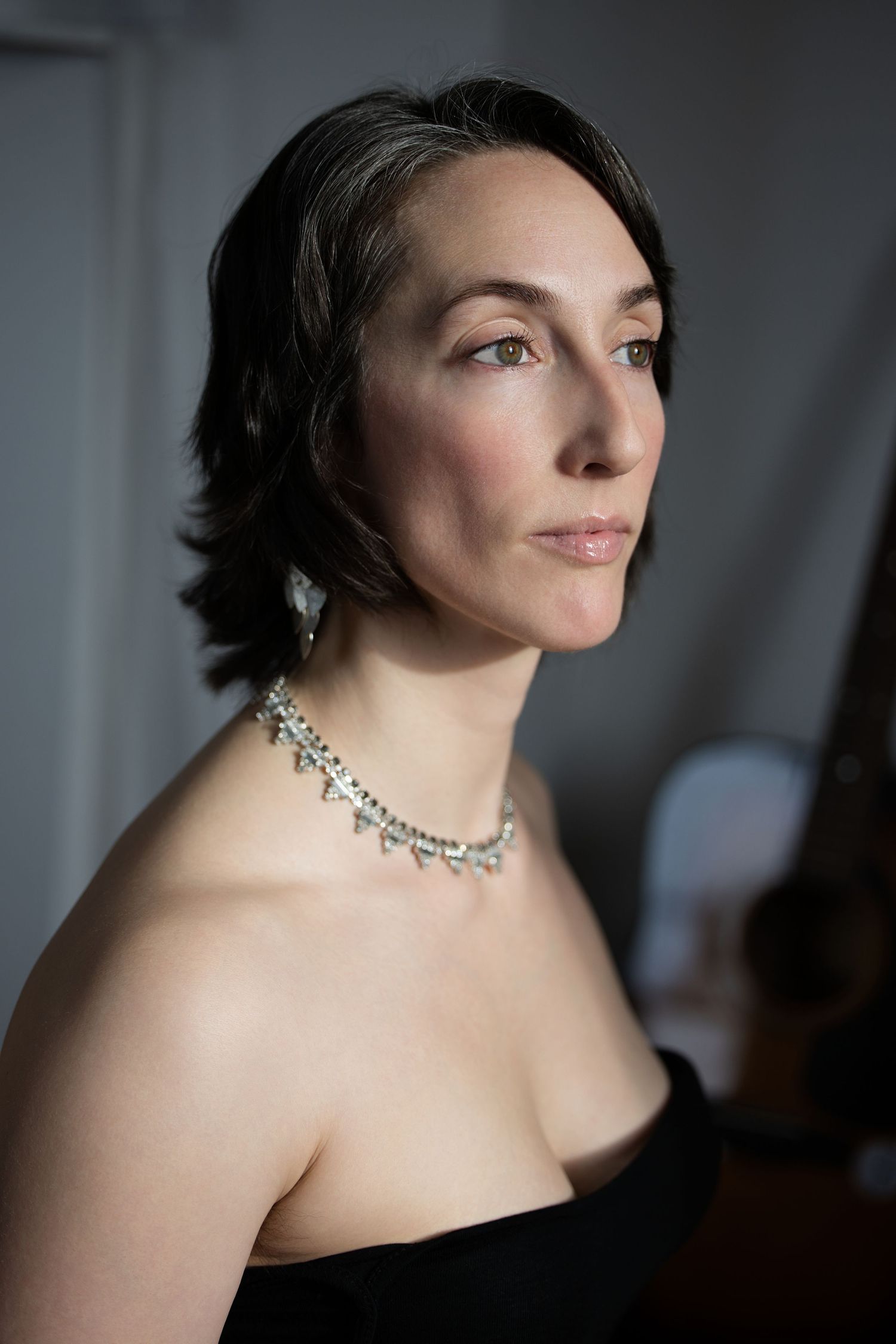 A close p of a white woman looking to the left of the camera in a black ball gown and nice necklace