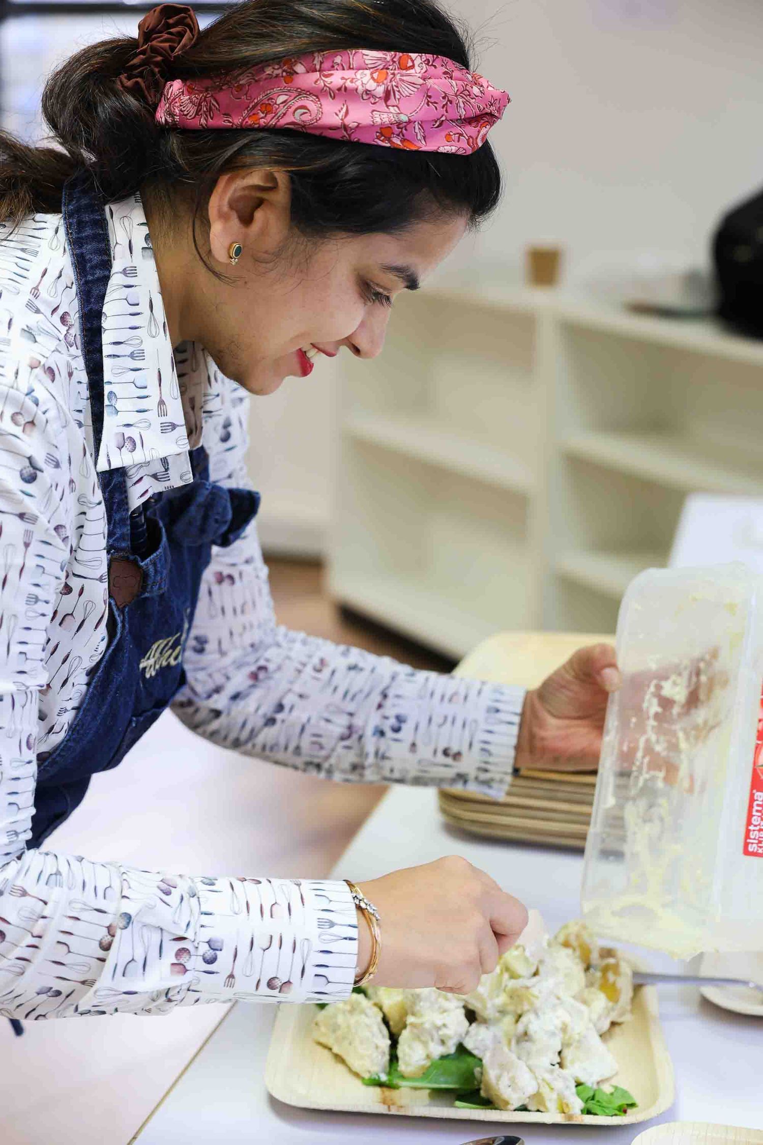 A female chef, with a pink headband, serving up Indian food onto a plate