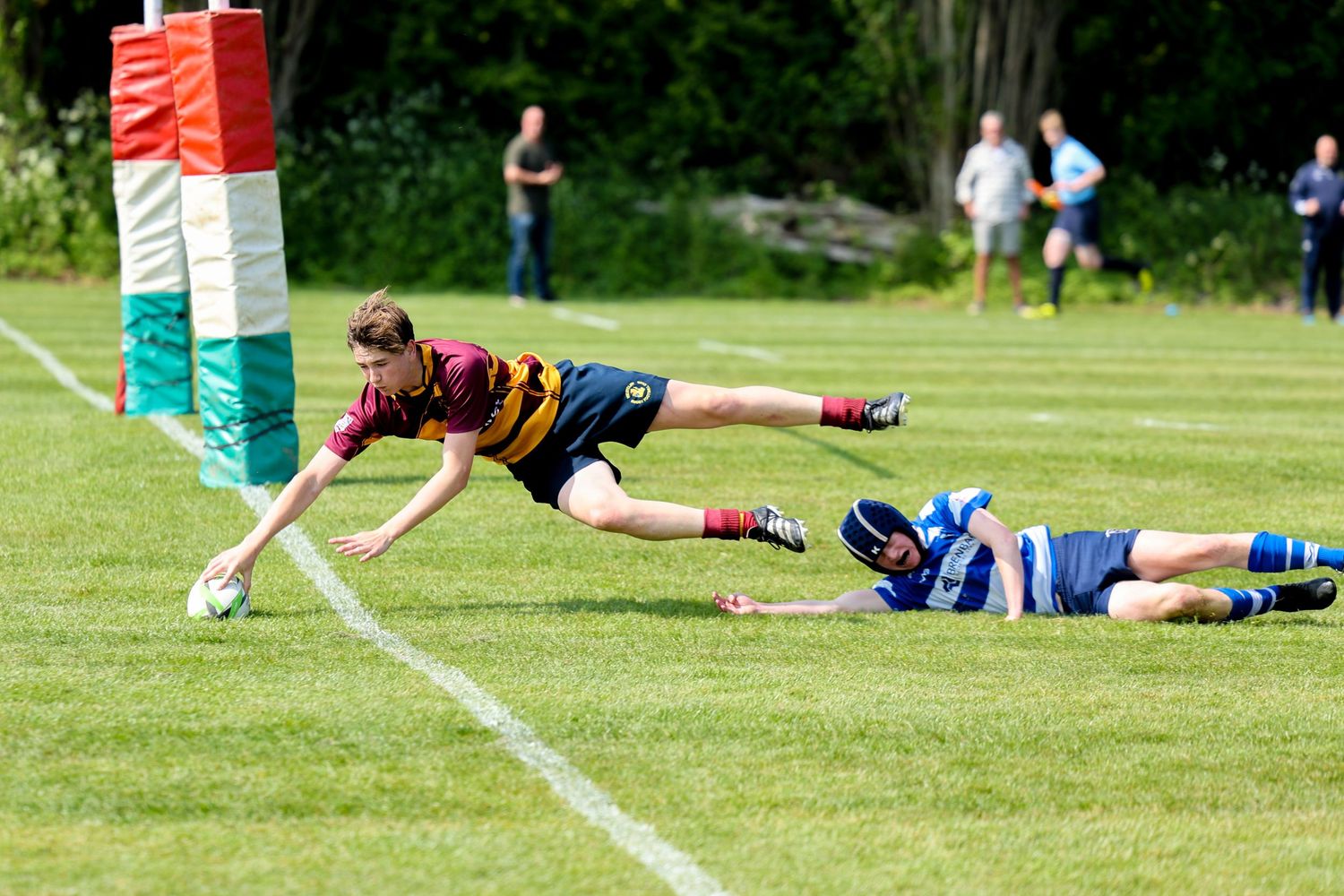 A boy diving for the try line to score a try as he places the ball down on the ground.