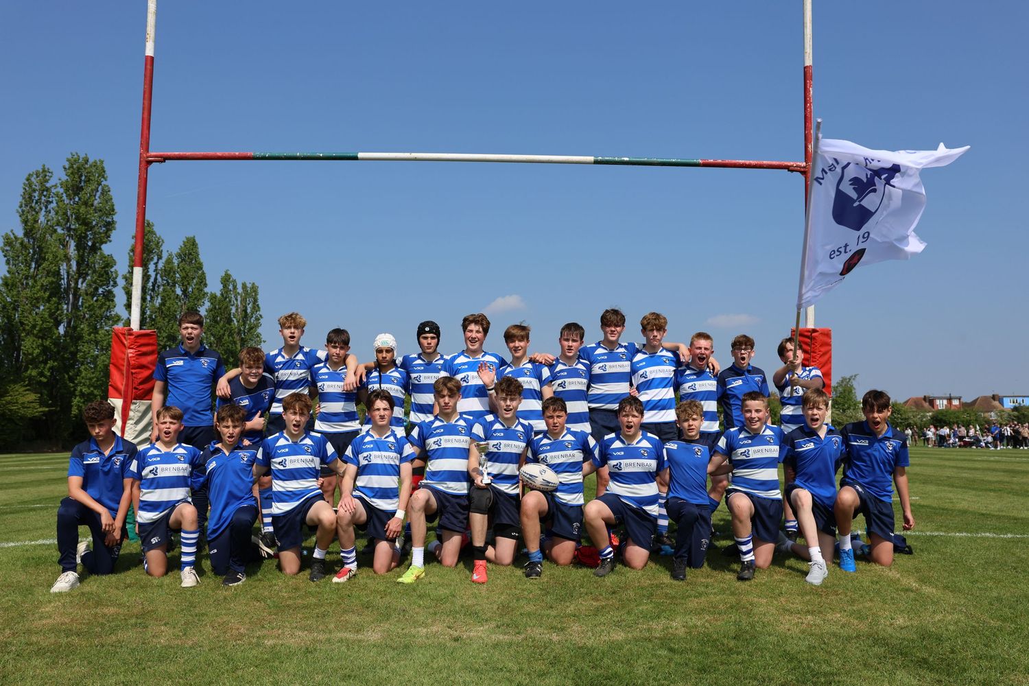 Rugby team picture of people in white and blue uniforms under the rugby post
