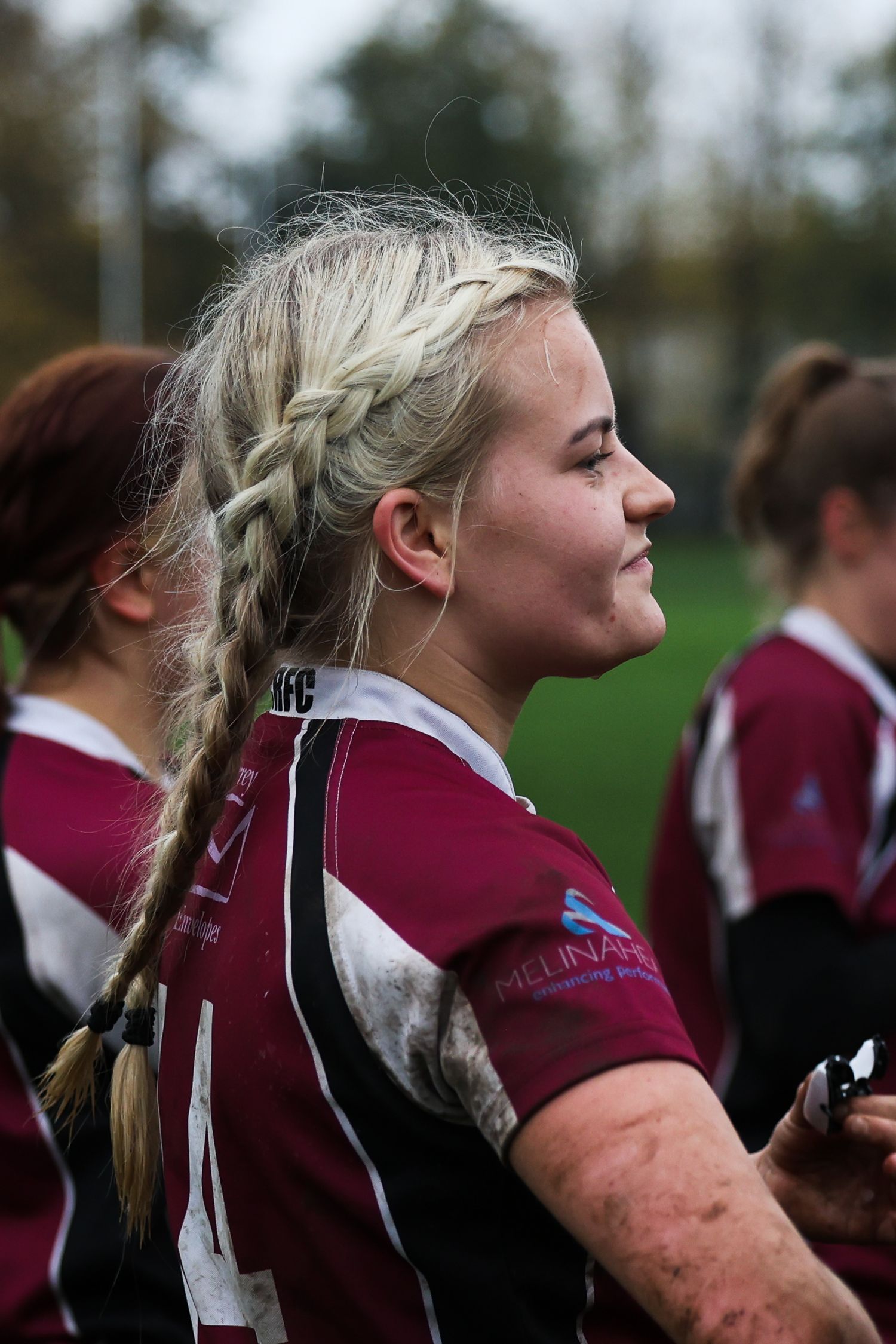 Close up of a woman with blond hair and muddy face listening to her coach give a team talk.