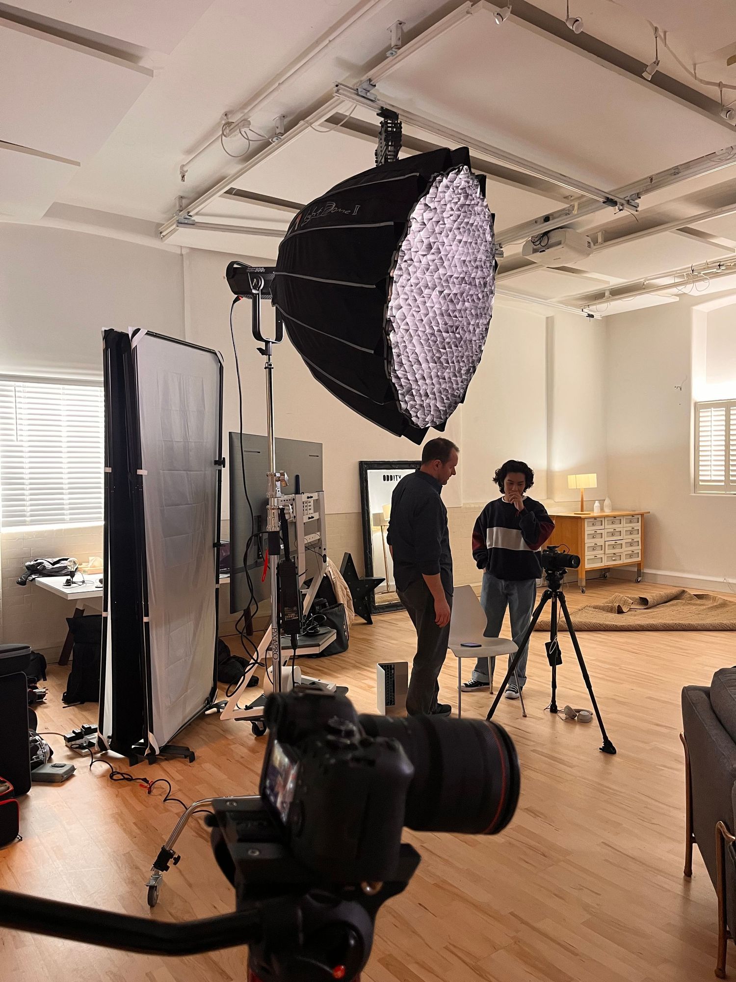 A large studio with overhead lights with 2 men gathered around a camera.