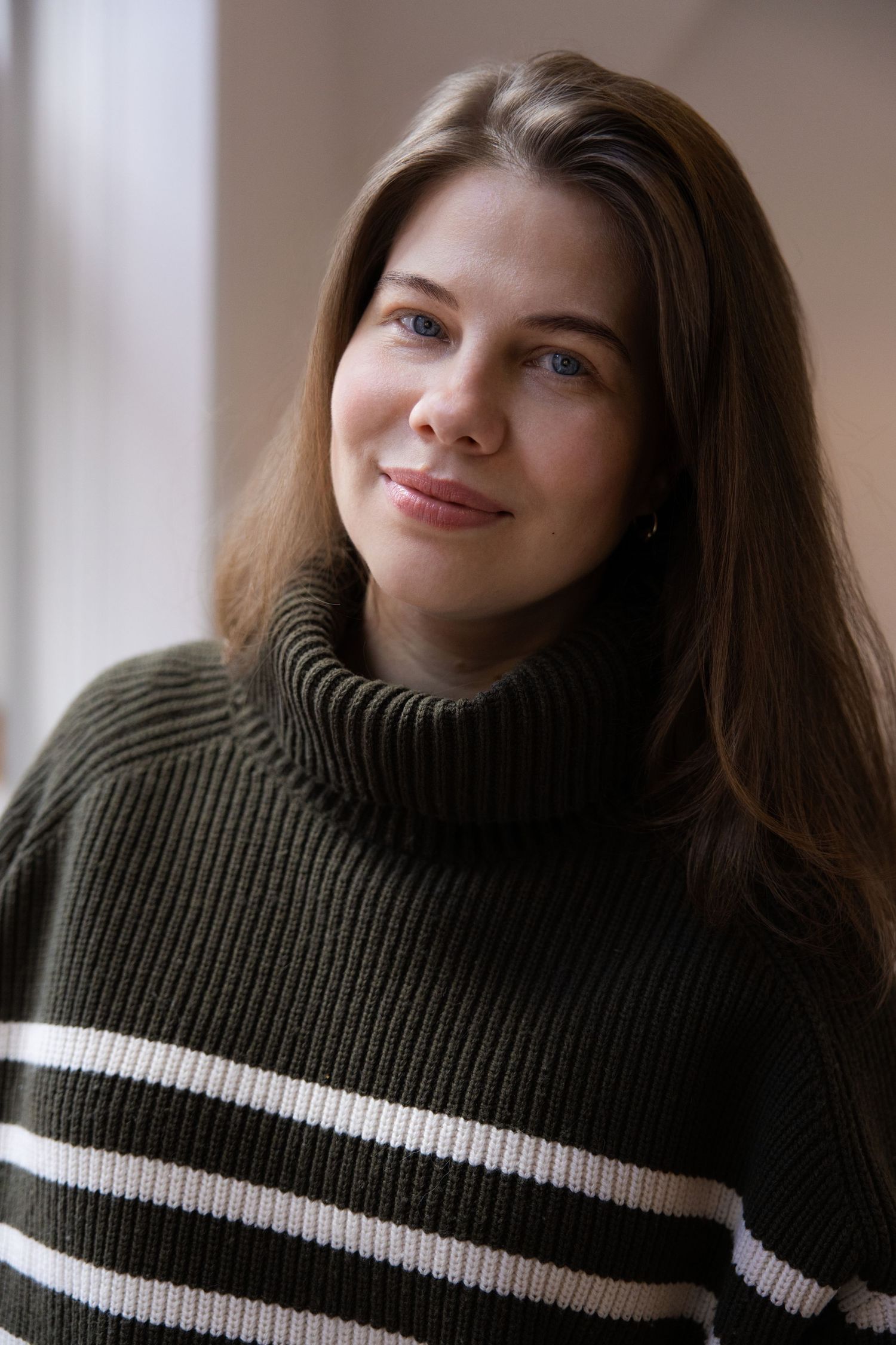 A woman with brown hair and a green and white striped jumper is smiling at the camera