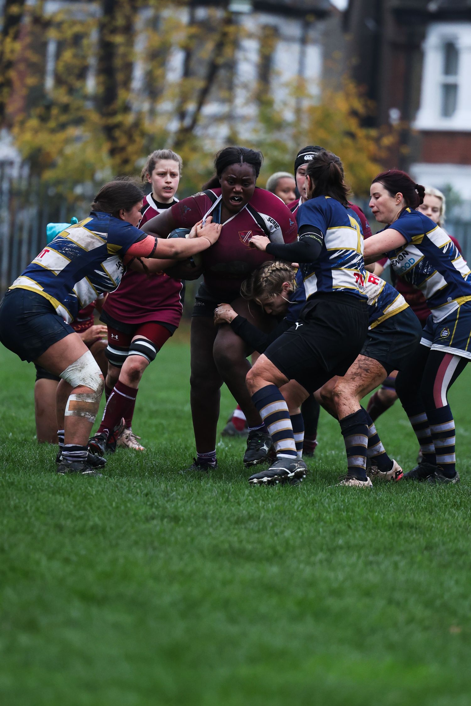 A woman pushing through 5 of her opponents in a woman's rugby game.