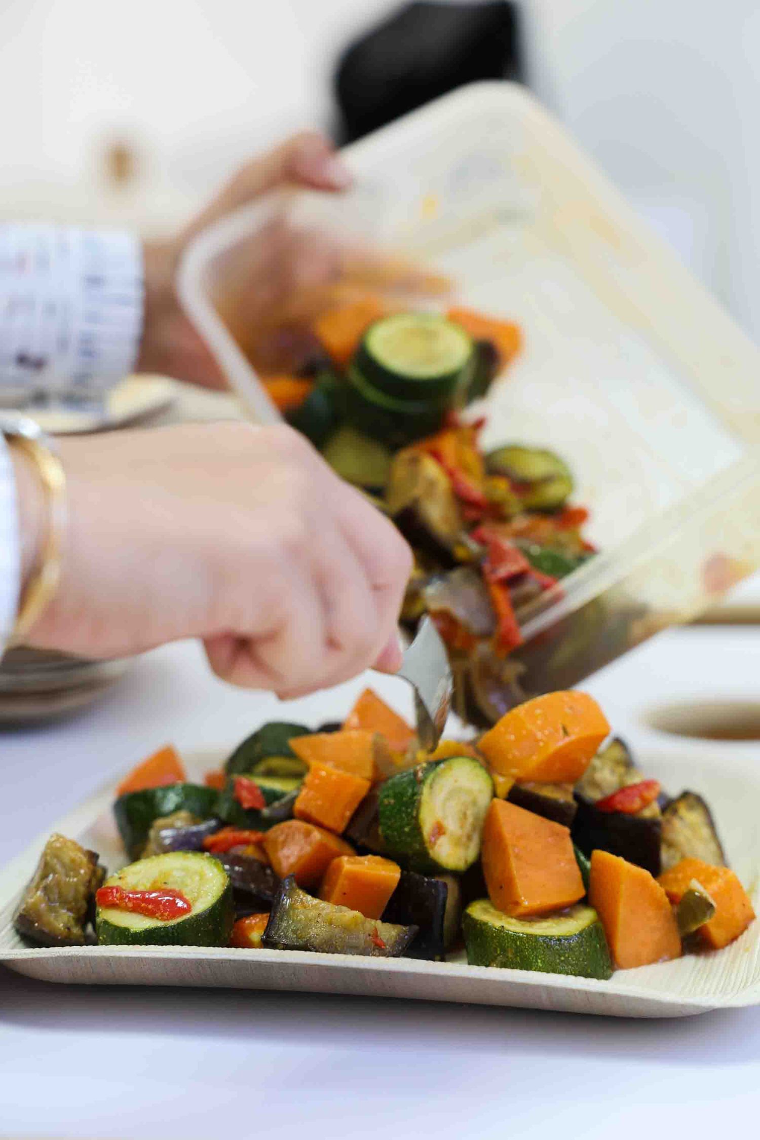A close up of a person distributing vegetarian food onto a plate