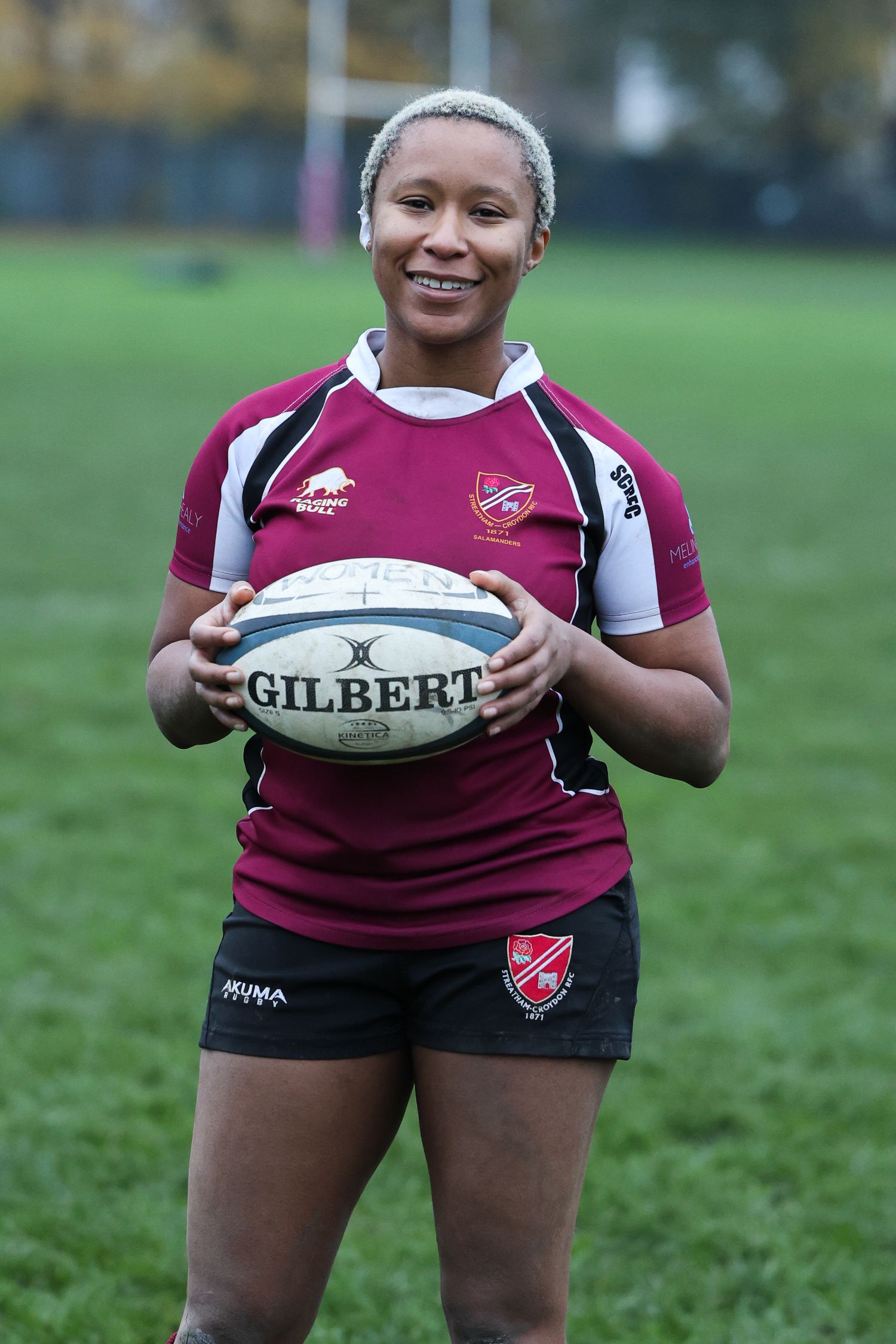 Portrait of a black woman with short bleached hair standing holding a rugby ball on the pitch