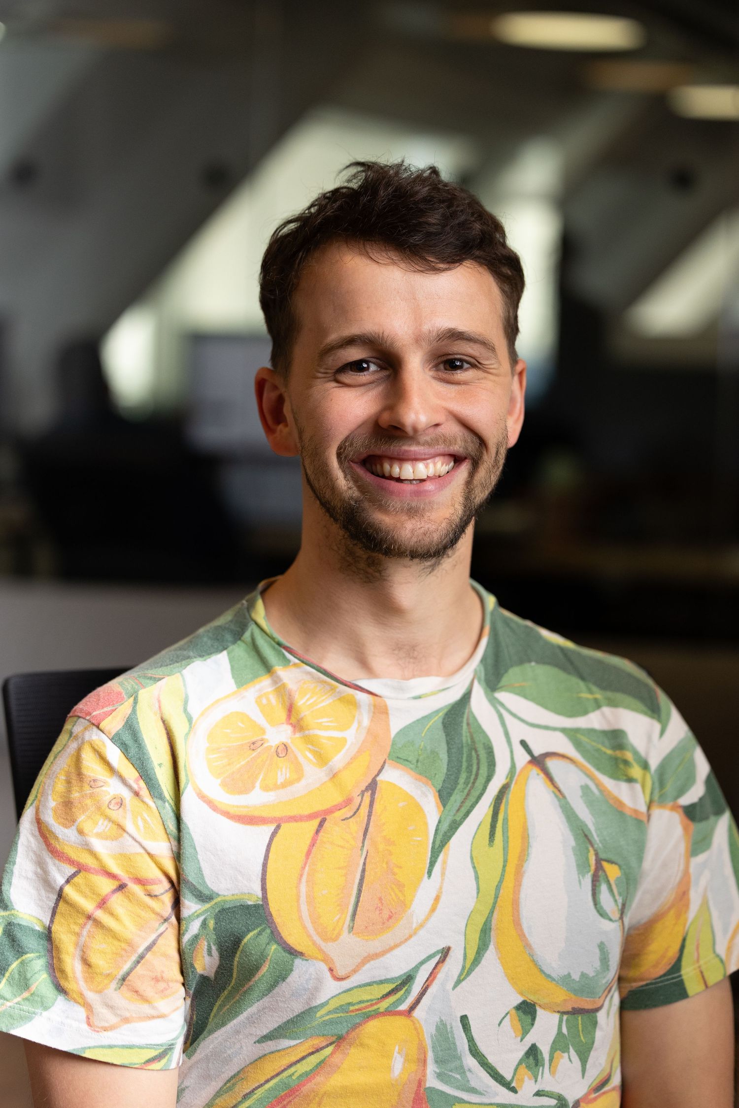 A head shot of a white man with a lemon tshirt with the office behind him