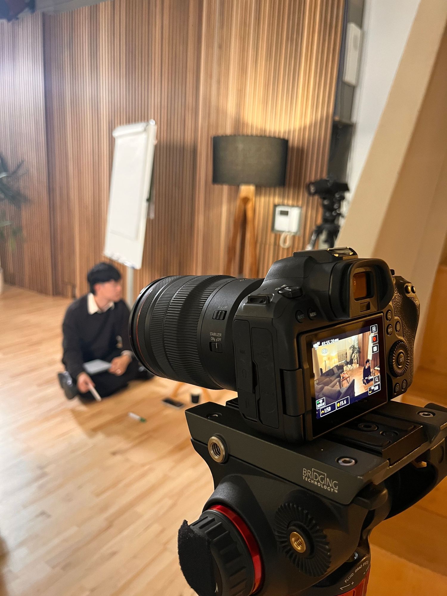 A picture of a camera on a tripod showing a person sat on the floor of a photography studio.