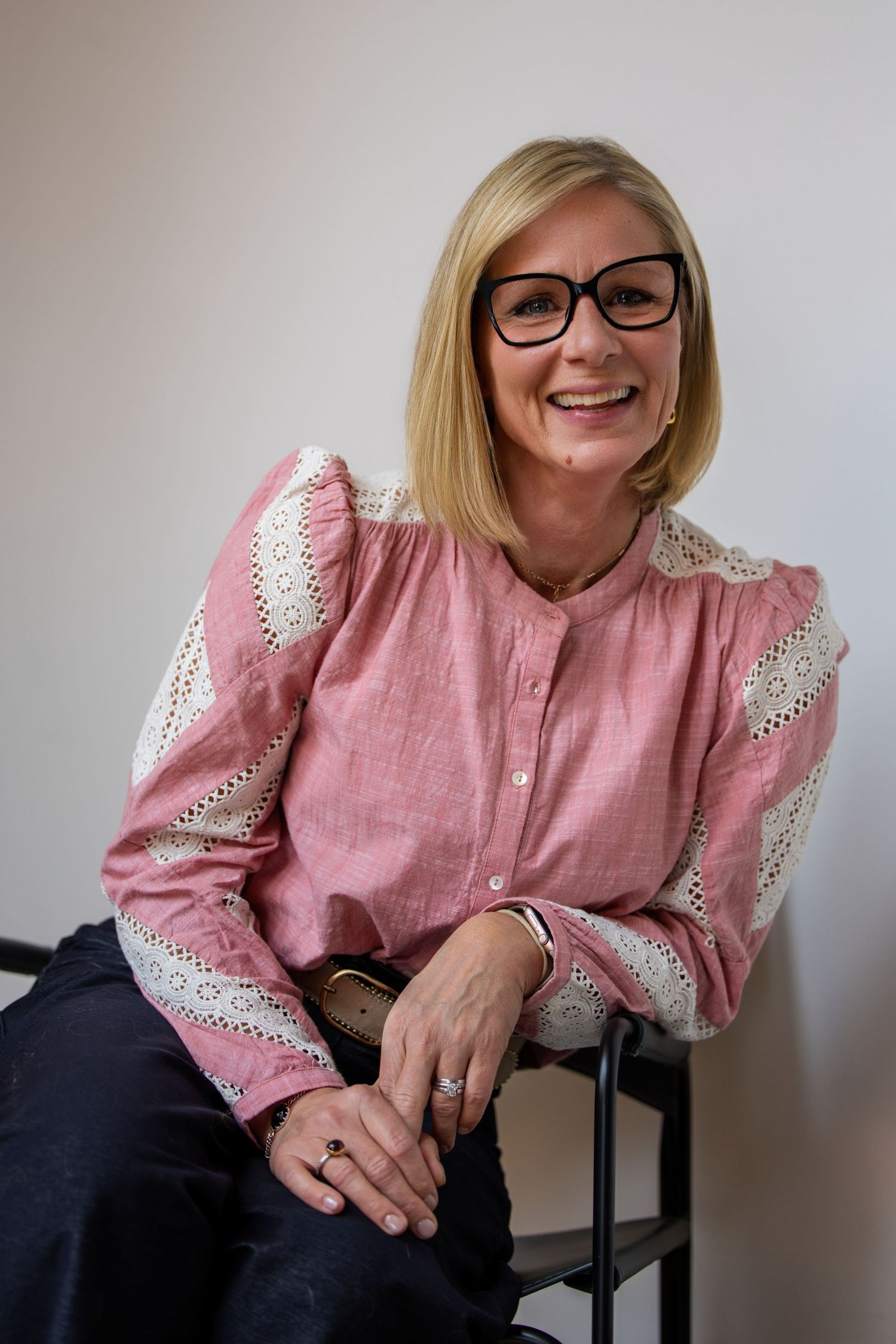 A white woman in a pink shirt leaning against the arm of her chair laughing