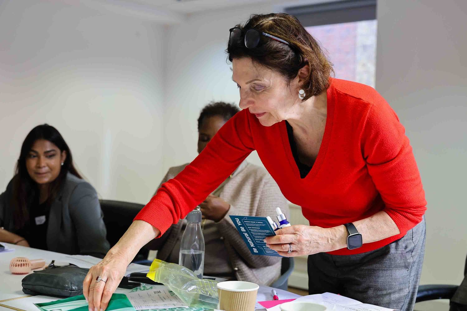 A woman in a red top learning over a table at a business meeting