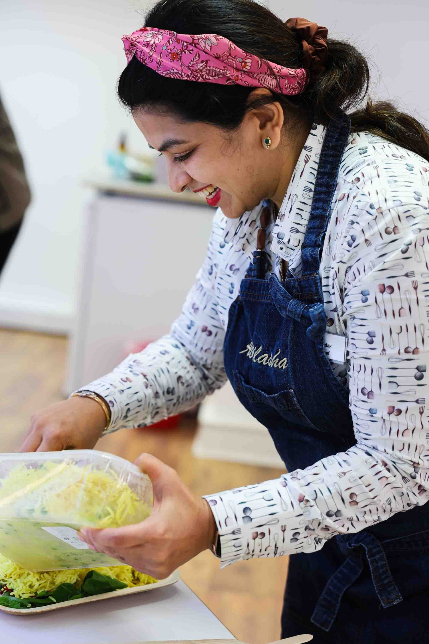 A female chef pouring out food while smiling - looking at the camera