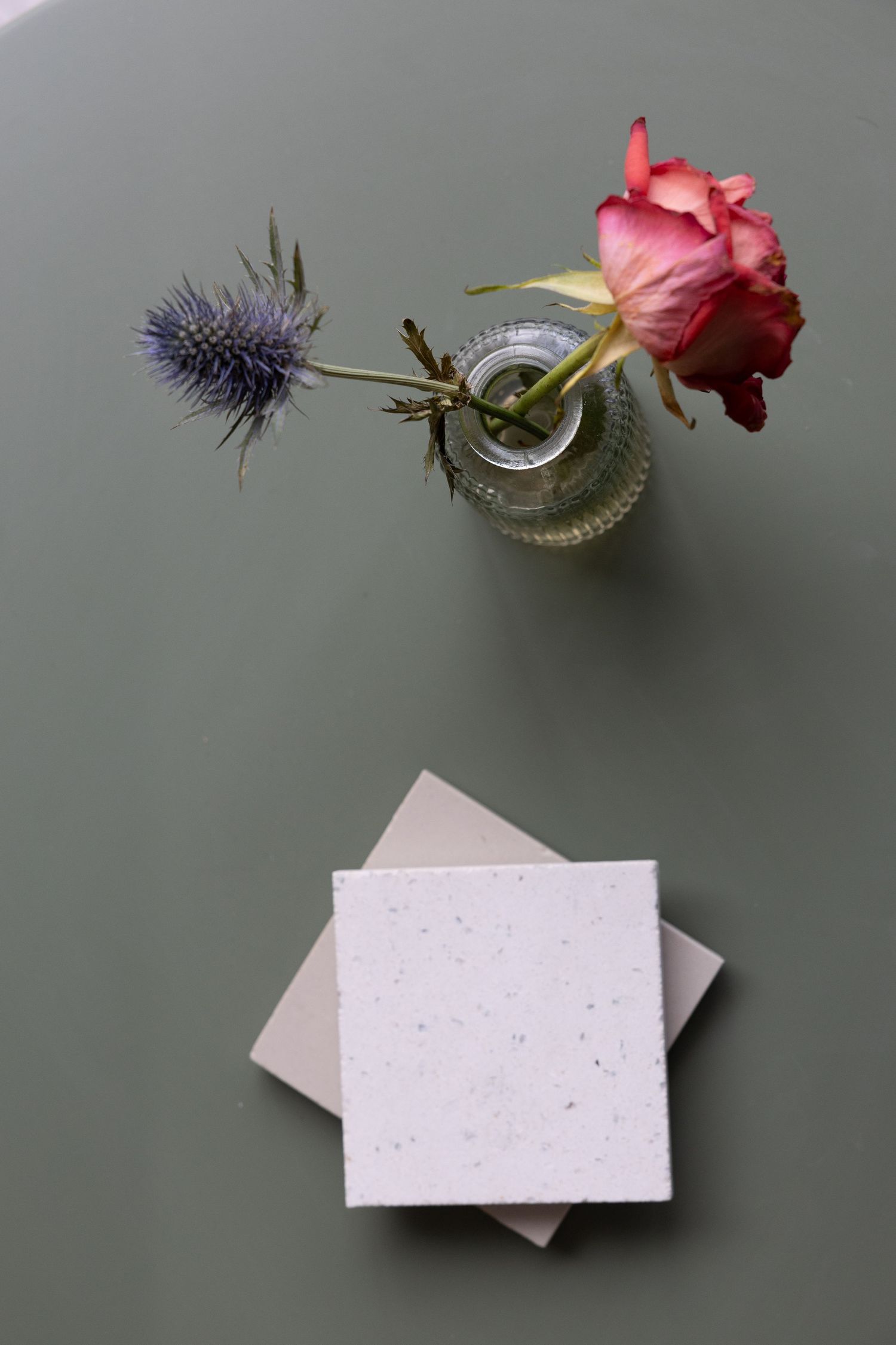 Photograph of rose and thistle in a jar next to coasters on a green background.