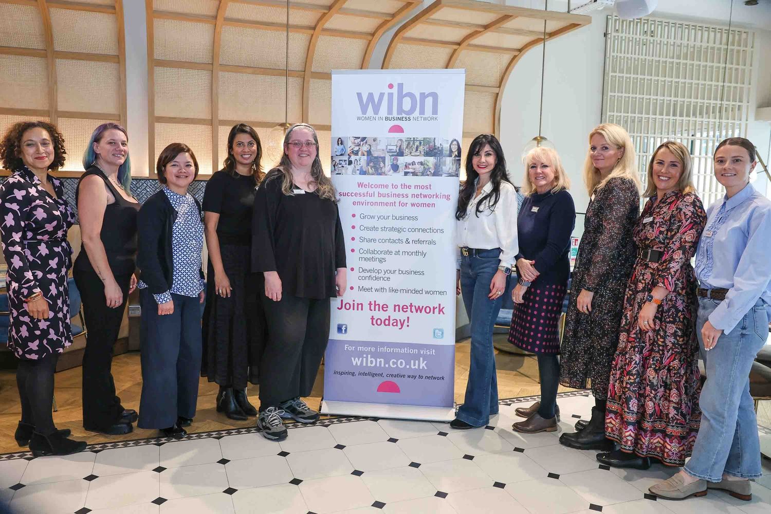 A tall pop up banner for Women In Business Network surrounded by women who attended the business network meeting