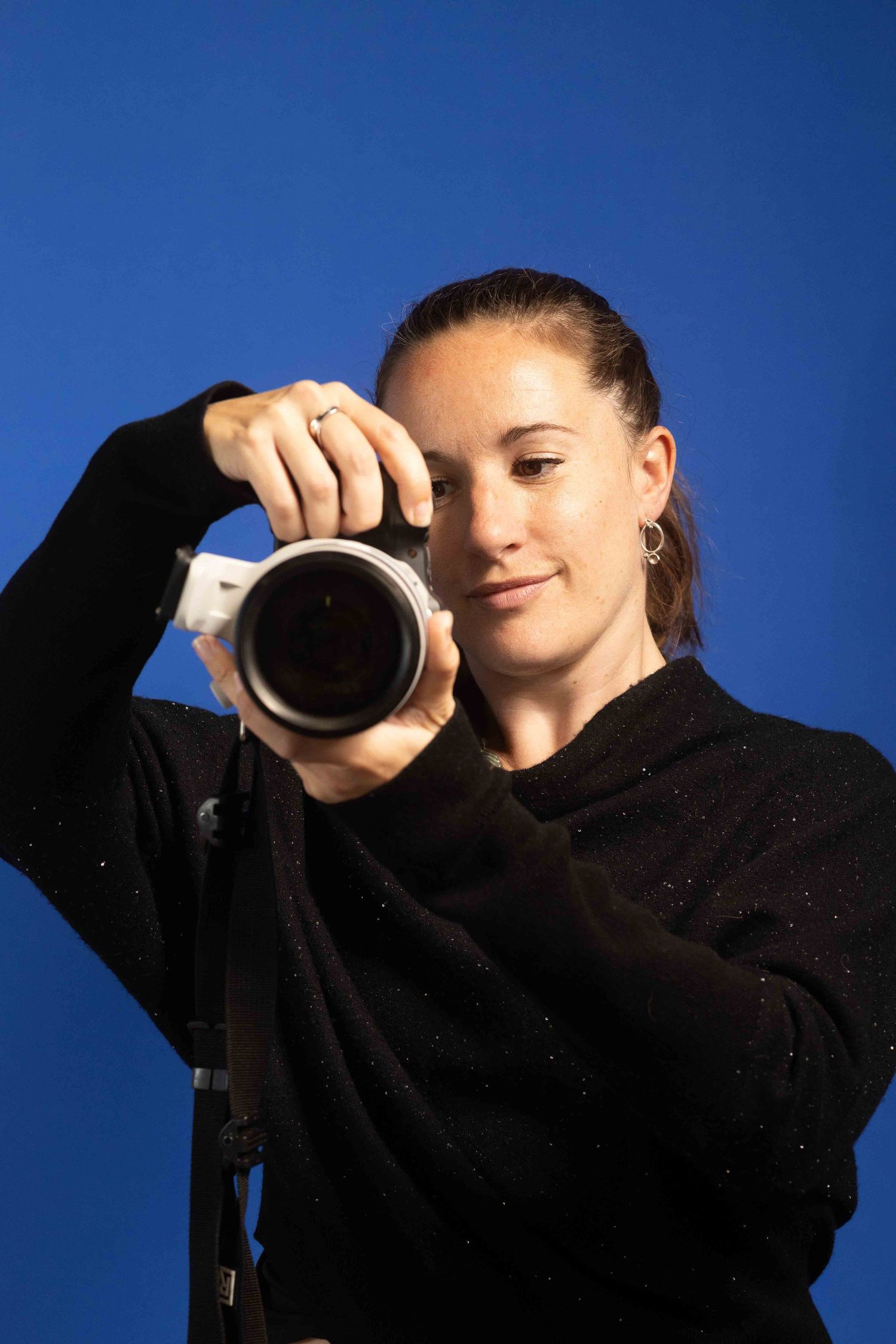 woman holding a camera looking through it on w a blue background