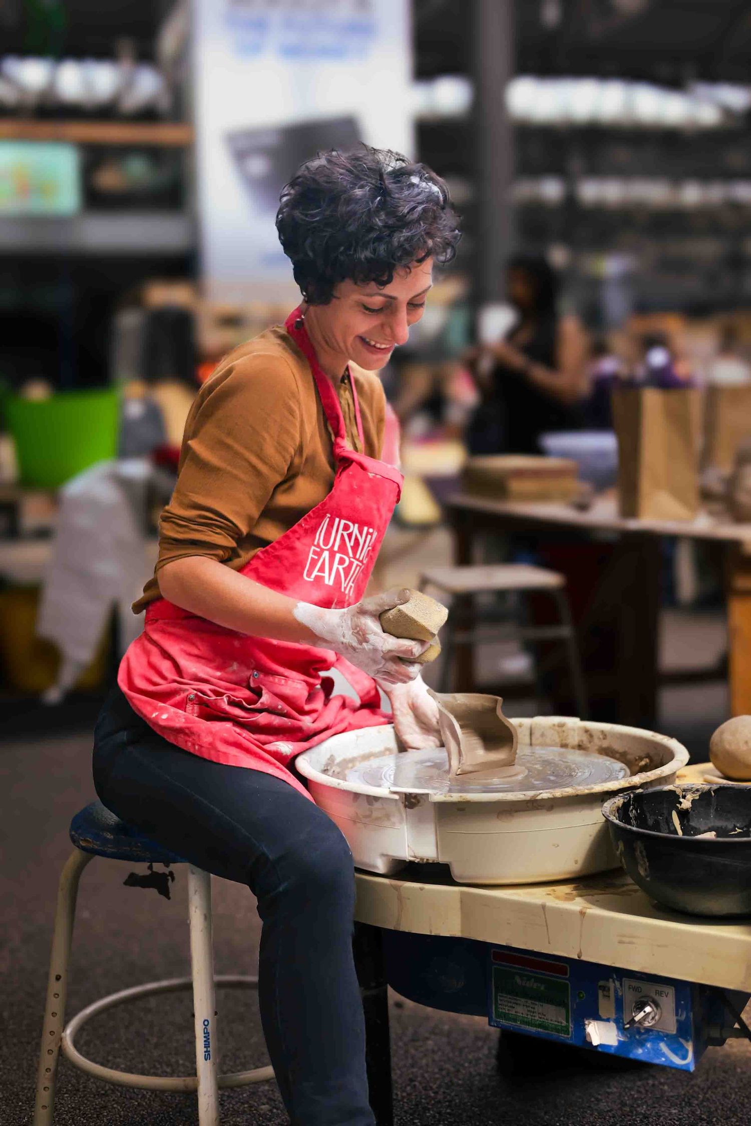 women in red apron is on a pottery wheel