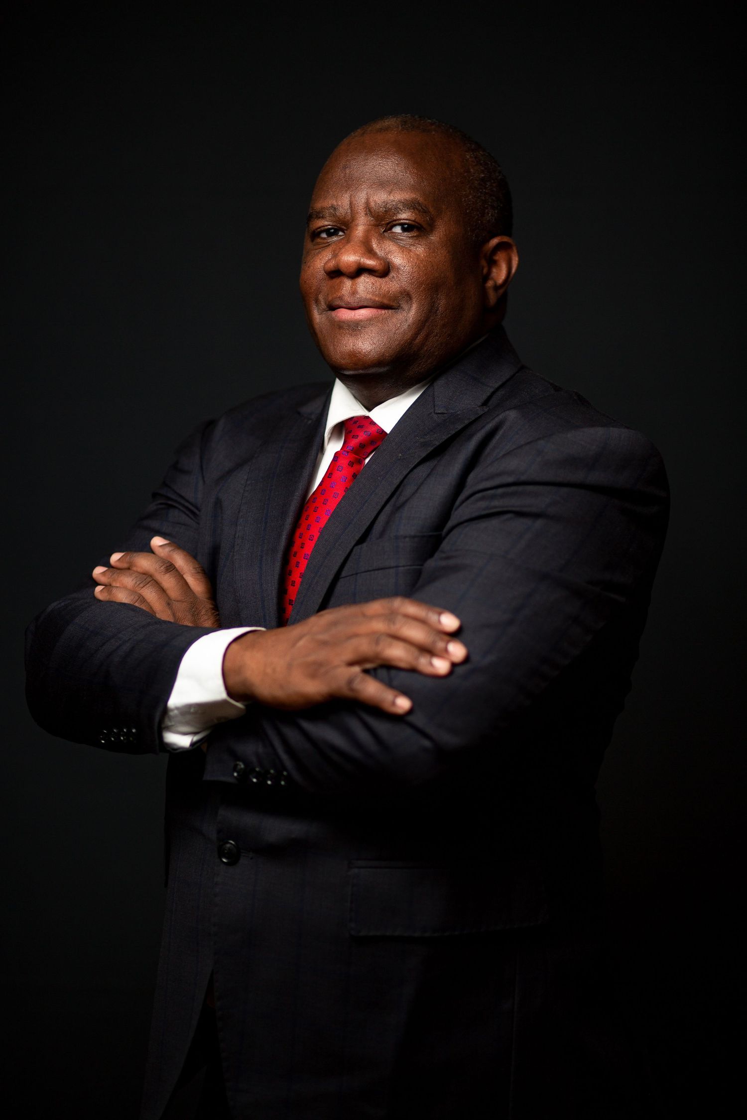 Professional portrait series showing confident poses in black suit with red tie against dark background.