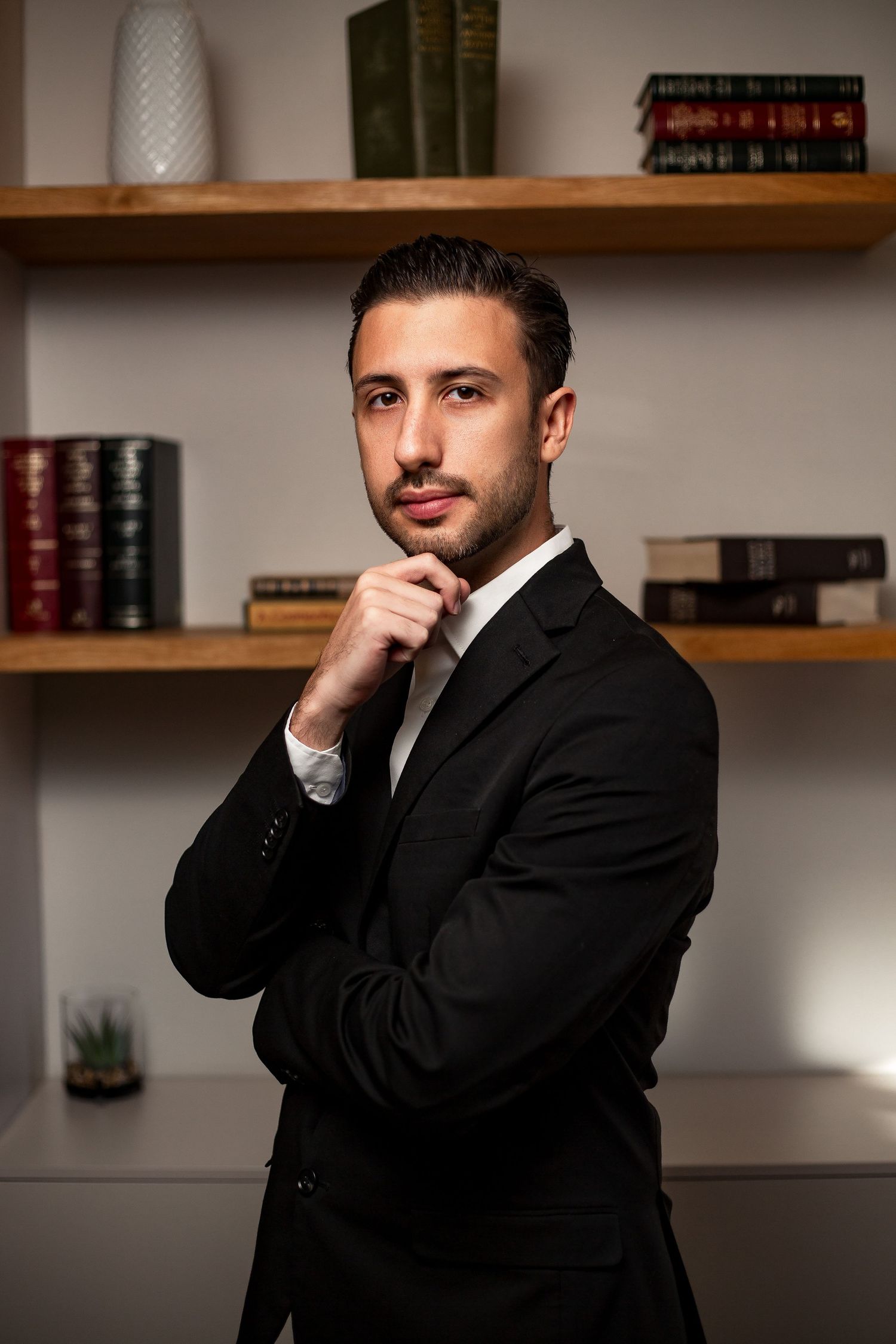 Series of professional portraits showing a person in dark suit against neutral background with wooden shelving.