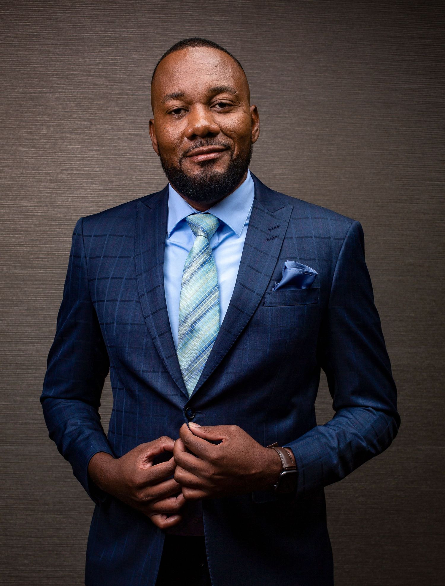 Business portraits featuring a person in navy suit and light blue tie against dark textured backdrop.
