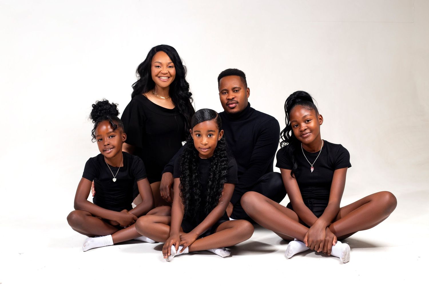 Family dressed in coordinated black outfits poses together for portrait on white background.