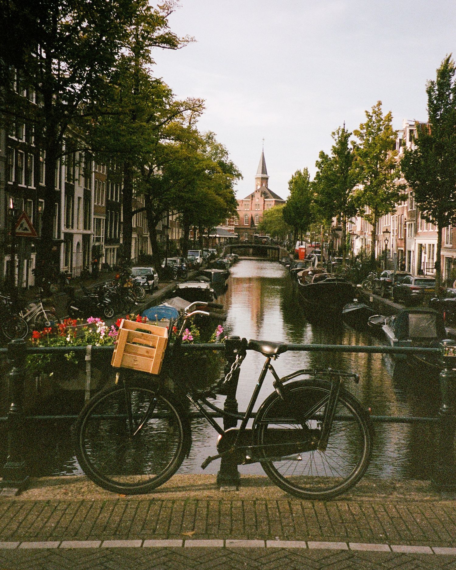 Film photograph of a scenic Amsterdam canal view showing historic buildings, parked bicycles, and boats along the waterway at sunset.