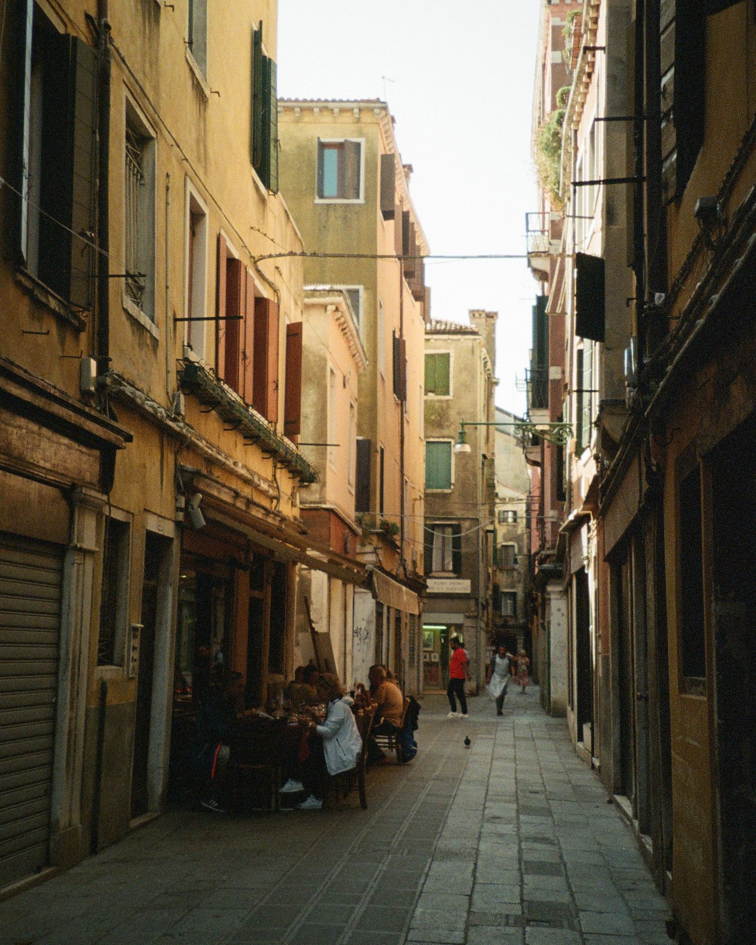 Film photograph of narrow cobblestone street lined with historic buildings and shuttered shops in Venice, Italy during daytime.