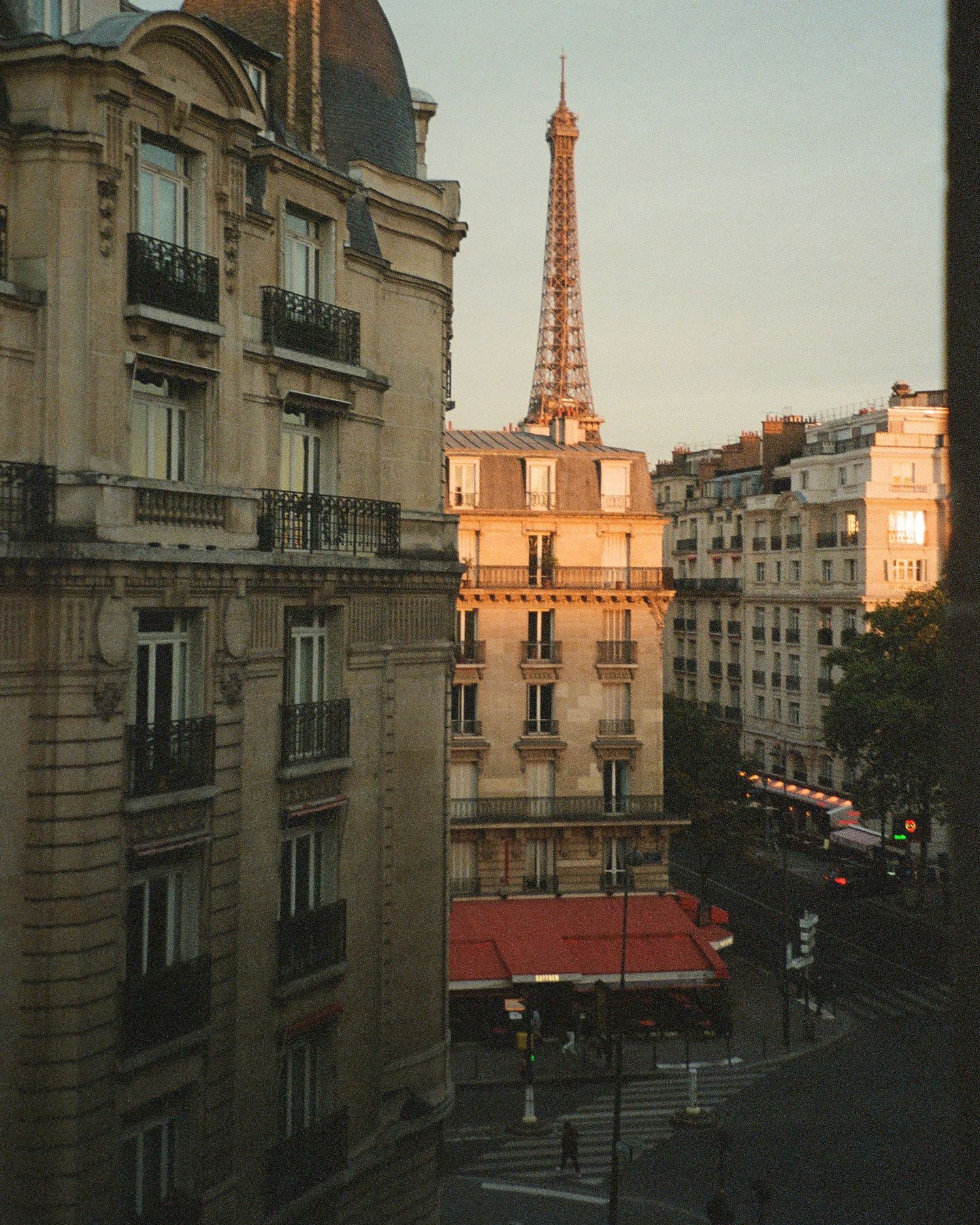 Film photography of view of the Eiffel Tower at sunset through Parisian buildings and streets in warm golden light.