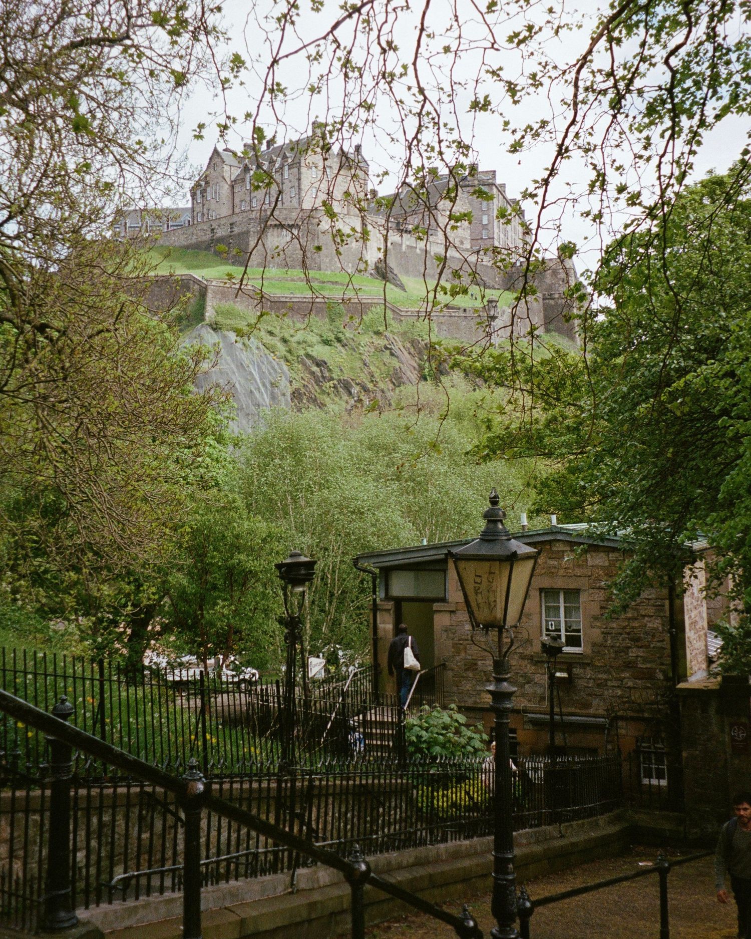 Film photograph of Edinburgh Castle and black iron railings line a tree-shaded path