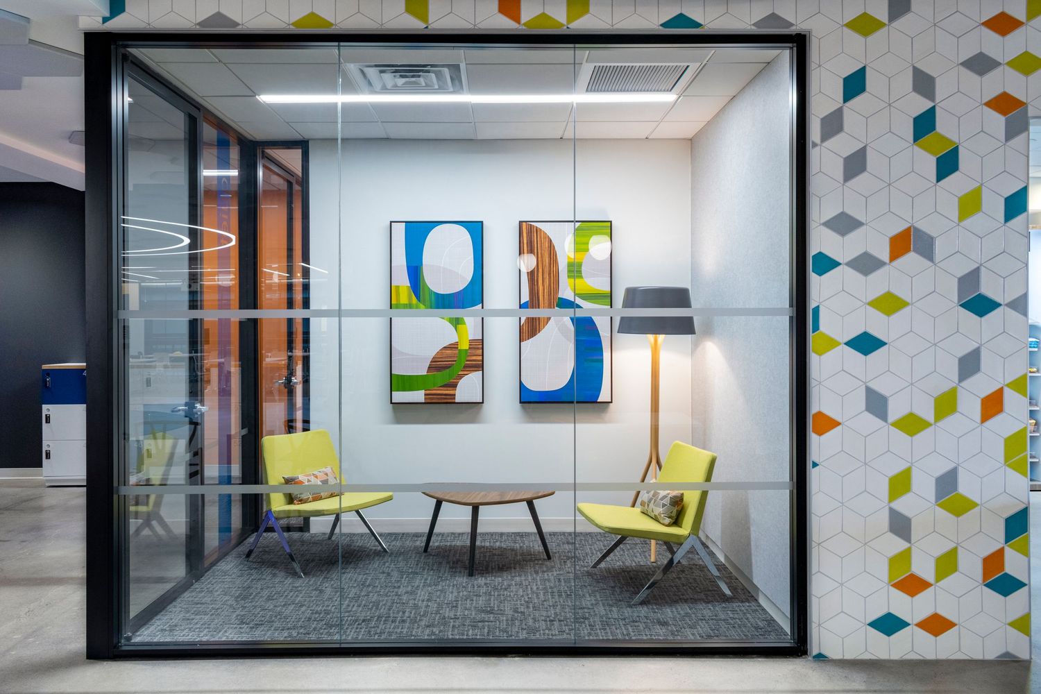 Modern office lounge with mid-century furniture, abstract wall art, and geometric tile wall accent in a commercial interior design setting.