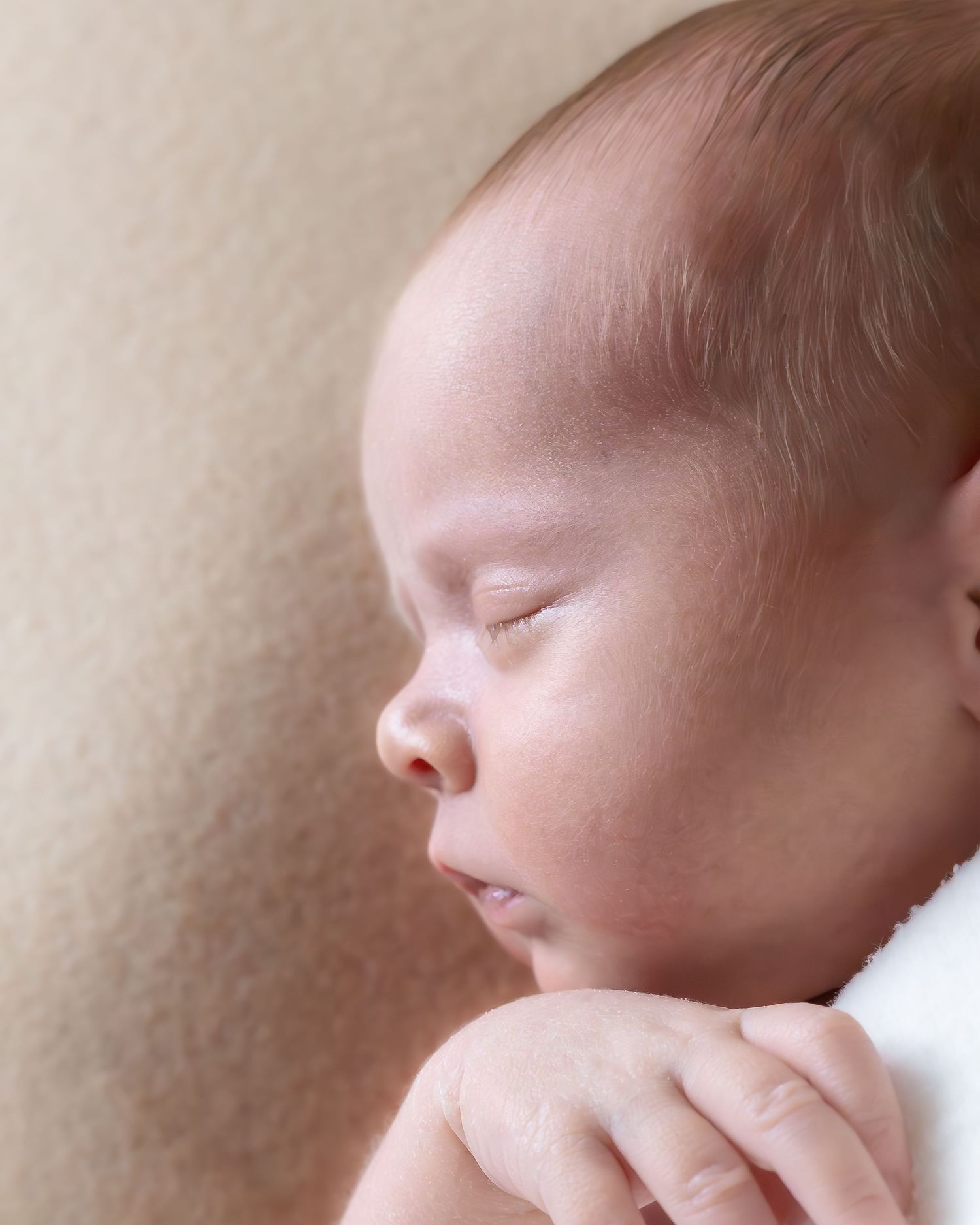 Peaceful sleeping newborn wrapped in cozy beige blanket showing gentle profile and tiny hand.