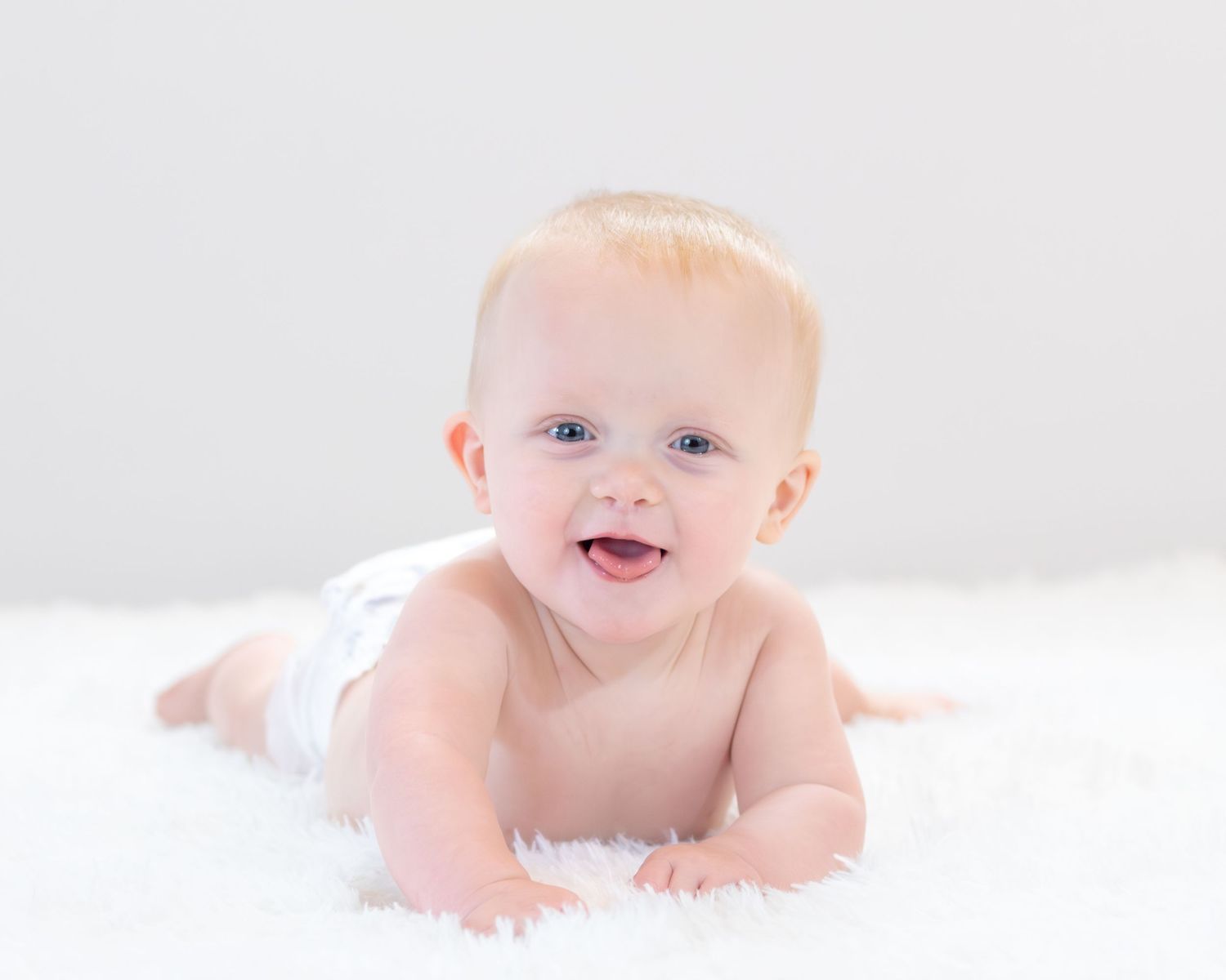 A smiling baby lying on their stomach on a white background.