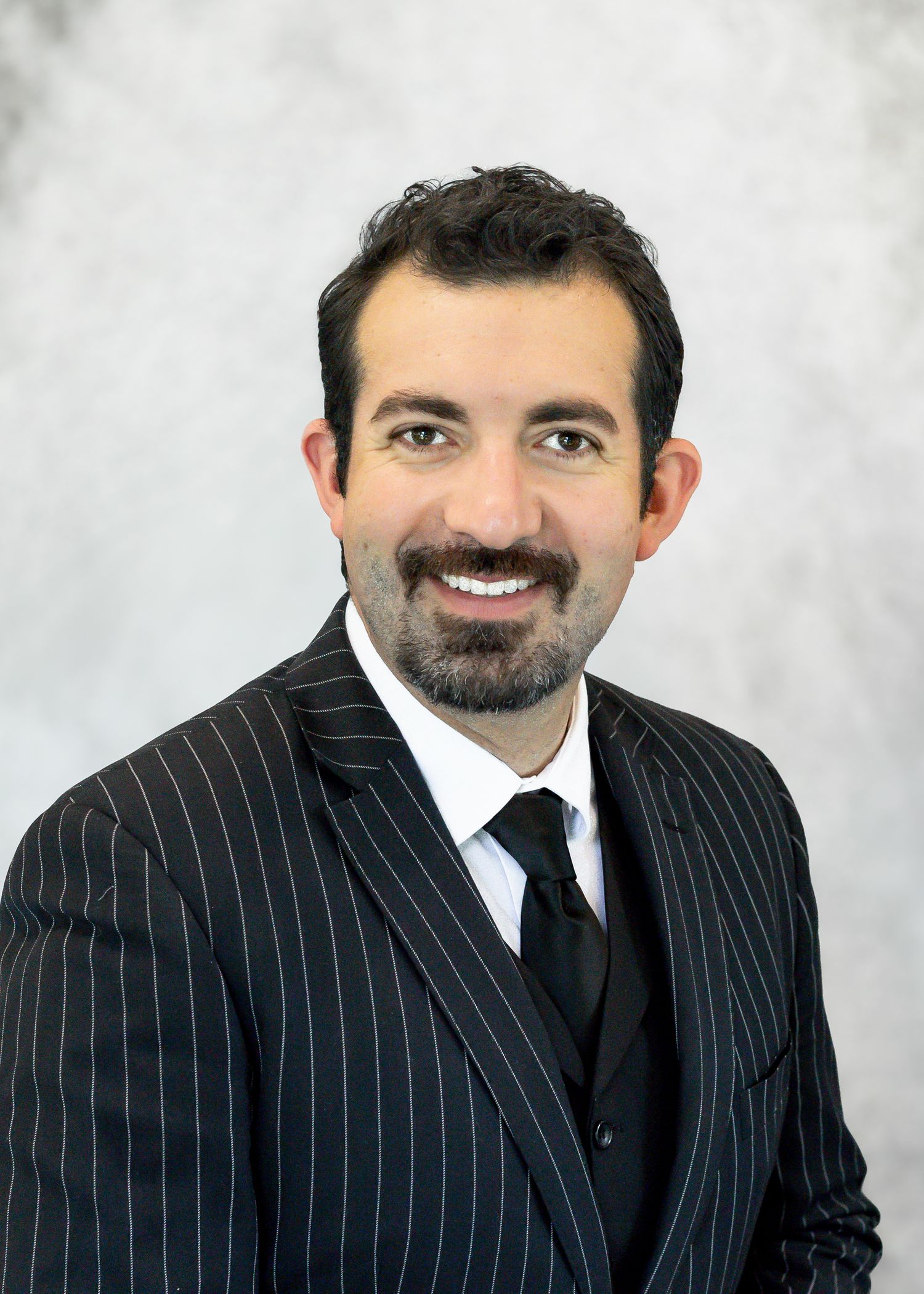 Professional man in pinstripe suit and black tie smiling for a formal business headshot photo.