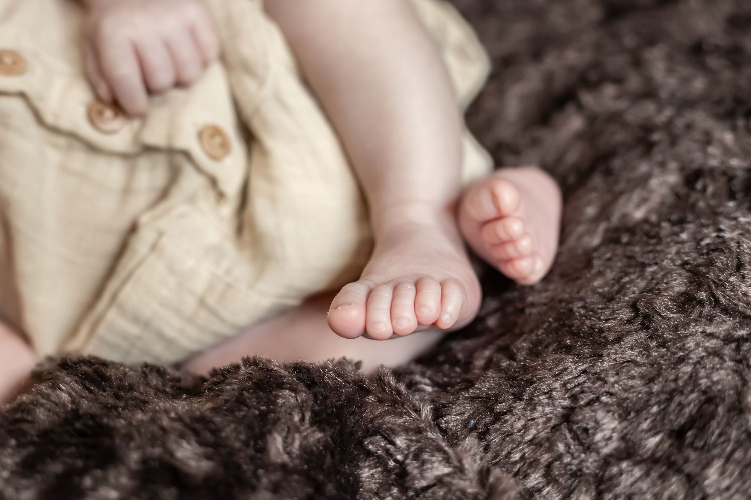 Close-up of tiny baby feet resting on dark textured blanket or rug.