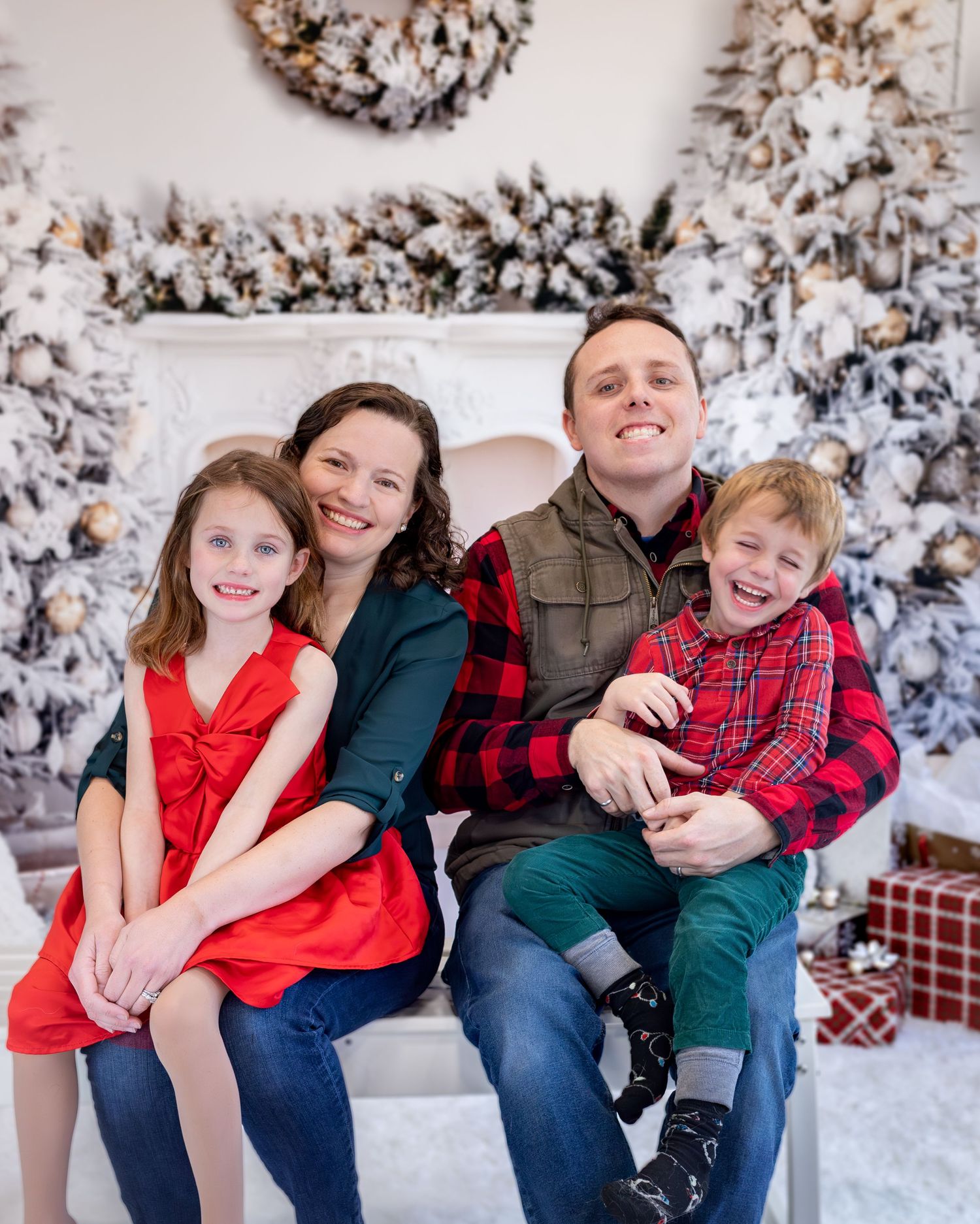 A family sits together on a bench in a winter scene with snow-covered trees in the background.