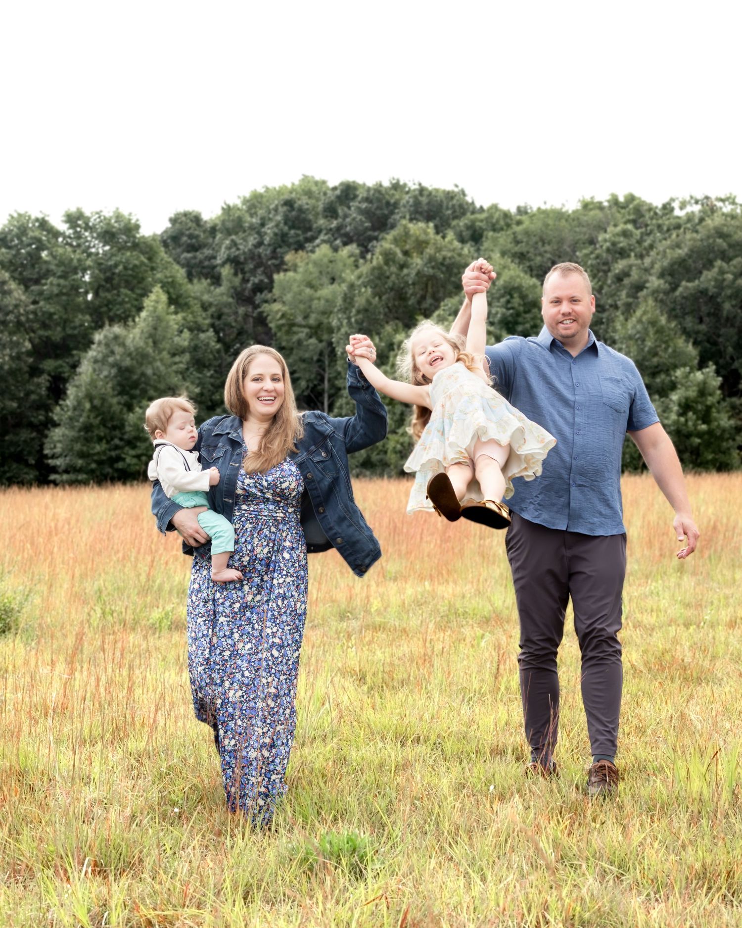 Family enjoying a playful moment together in a golden field with trees in the background.