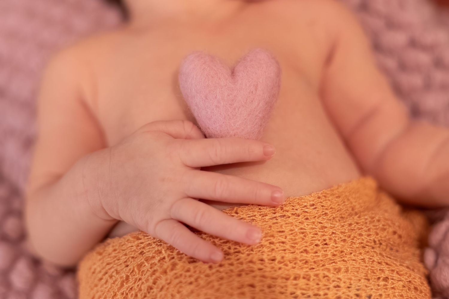 Hands gently hold and explore a soft, orange knitted or crocheted textile material.