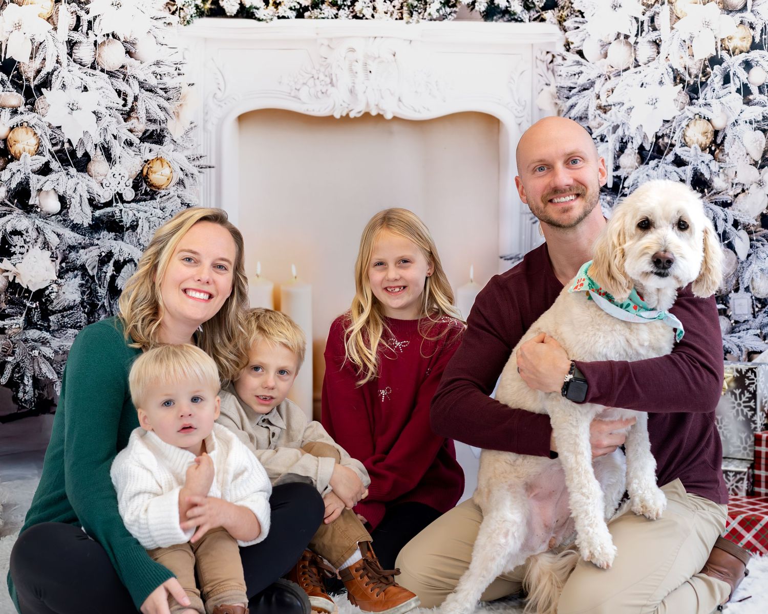 A family poses with their white fluffy dog on a couch during a holiday photo session with snowy decorations.
