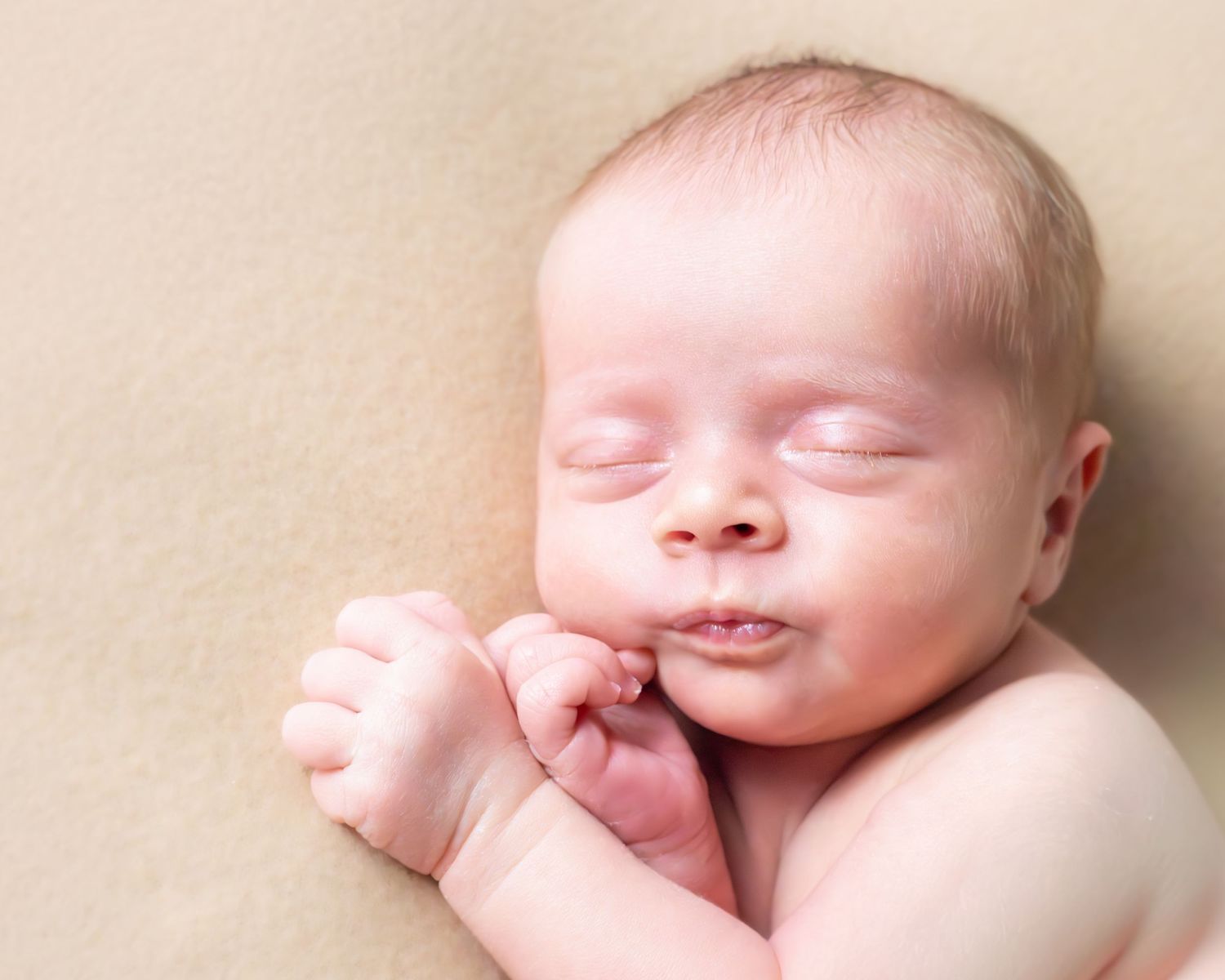 Close-up portraits of a sleeping newborn baby with delicate features against a soft beige background.