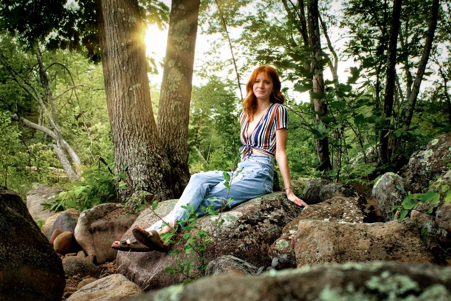 senior photography, girl sitting on rocks with sun flaring in the background