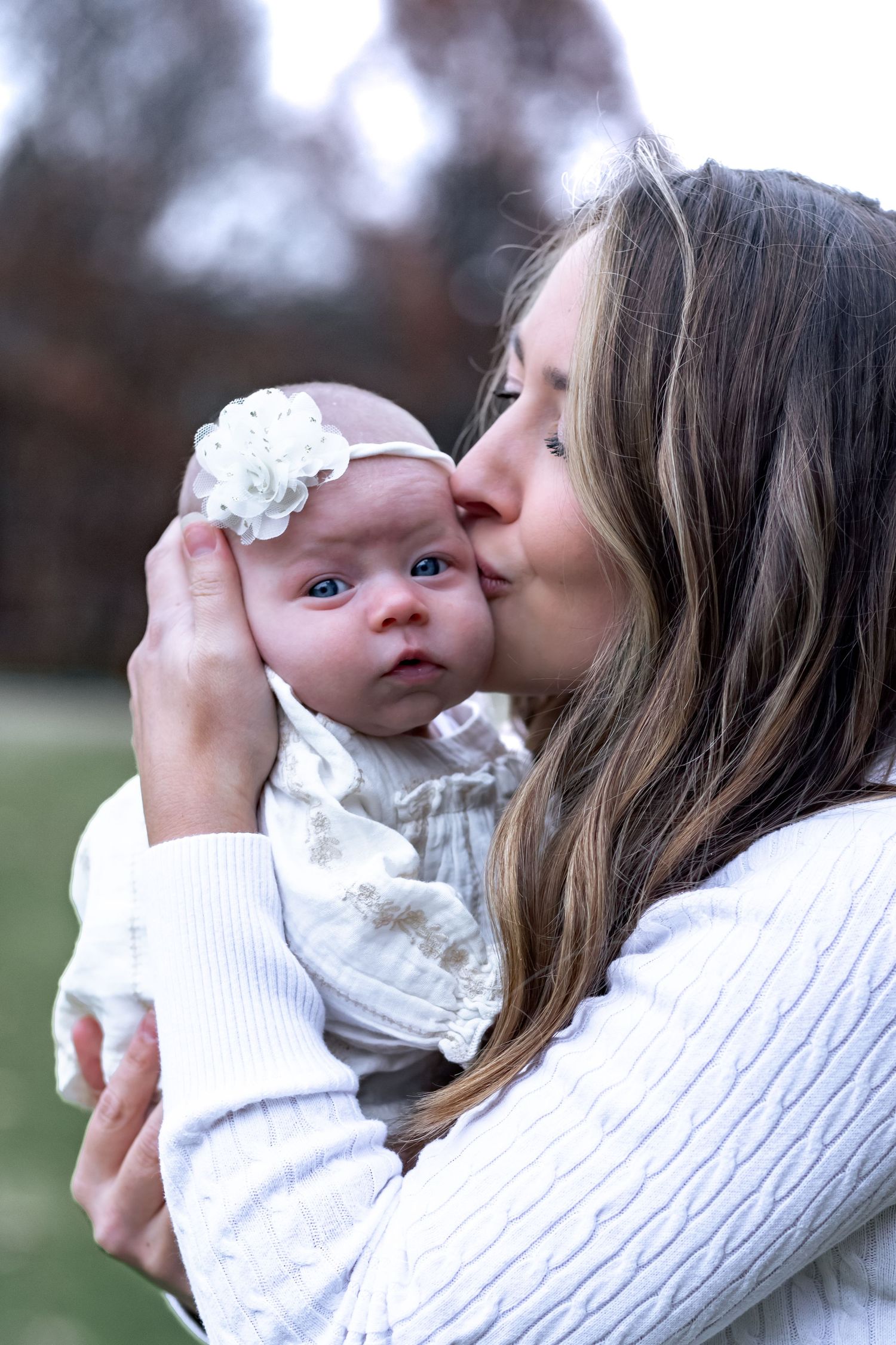 A tender moment captured in a series of photos showing a parent holding and kissing a baby wearing a white lace dress.