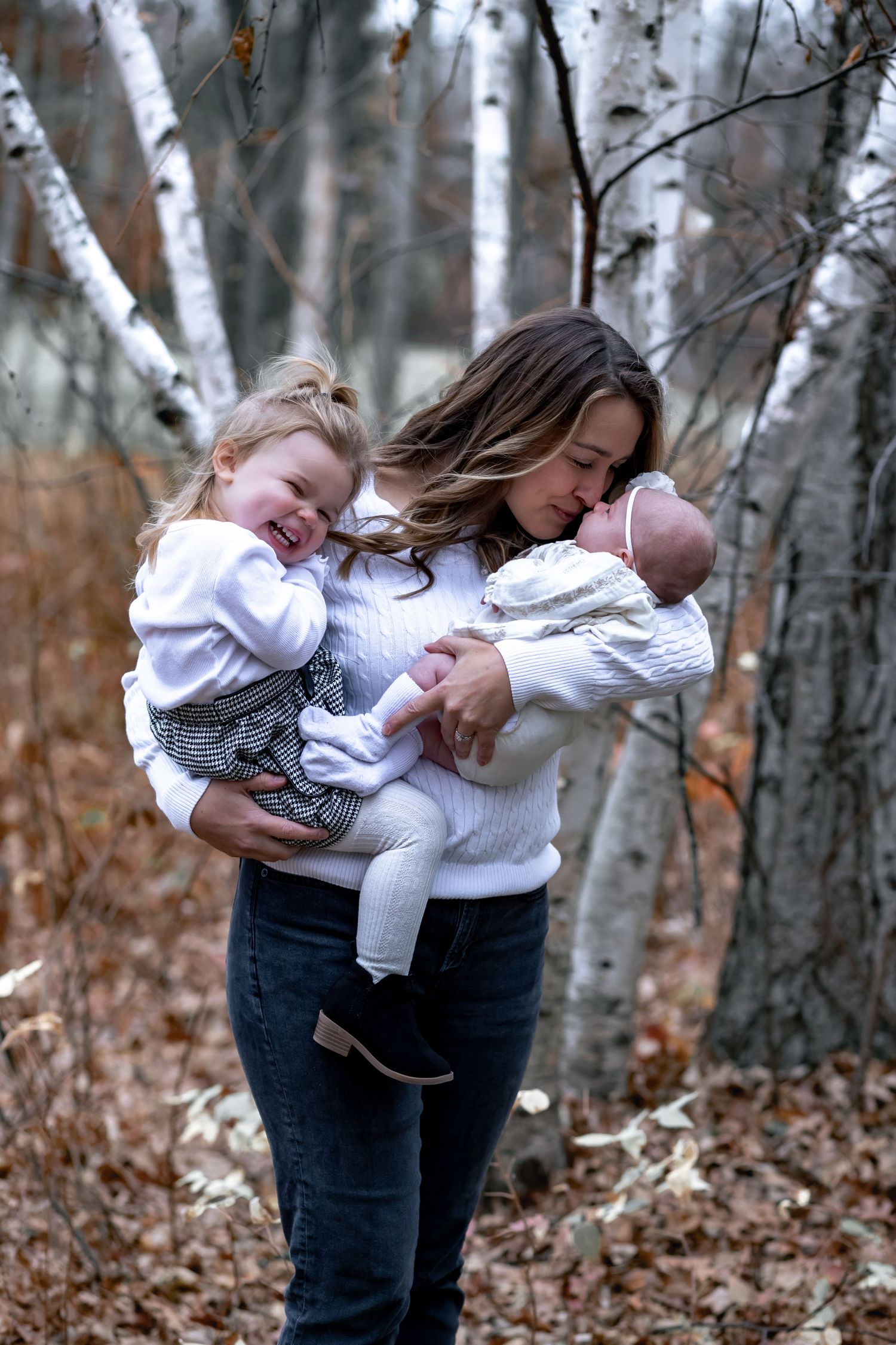 A candid family moment captured in a birch forest during autumn, showing tender interaction between parent and children.