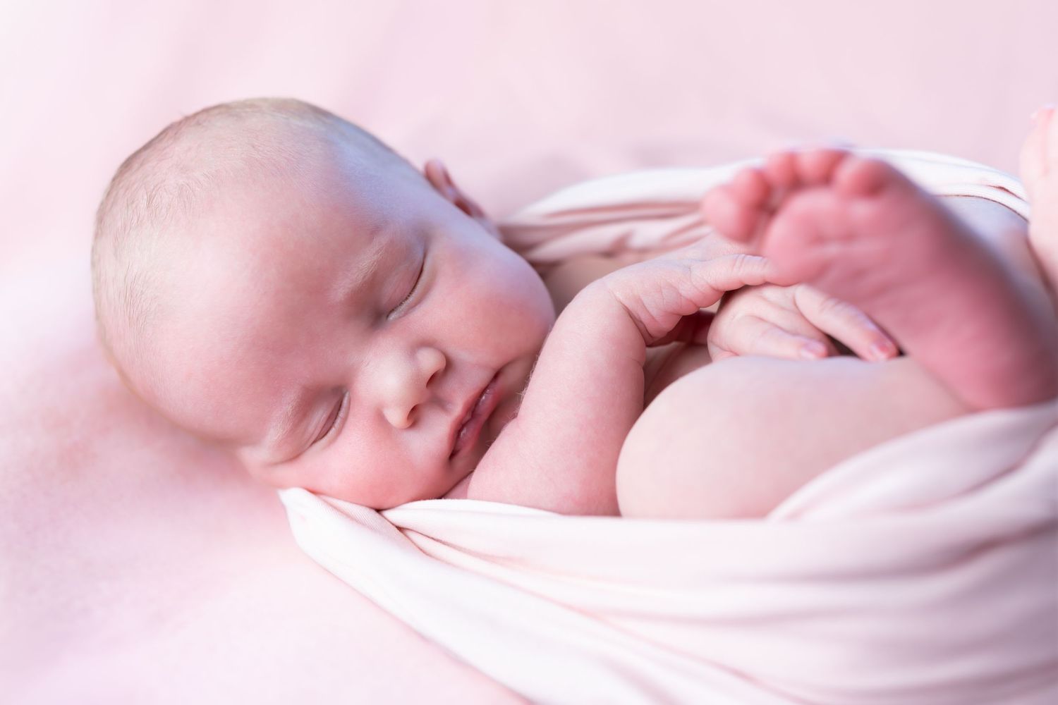 Peaceful sleeping newborn baby swaddled in soft pink blanket with delicate lighting.