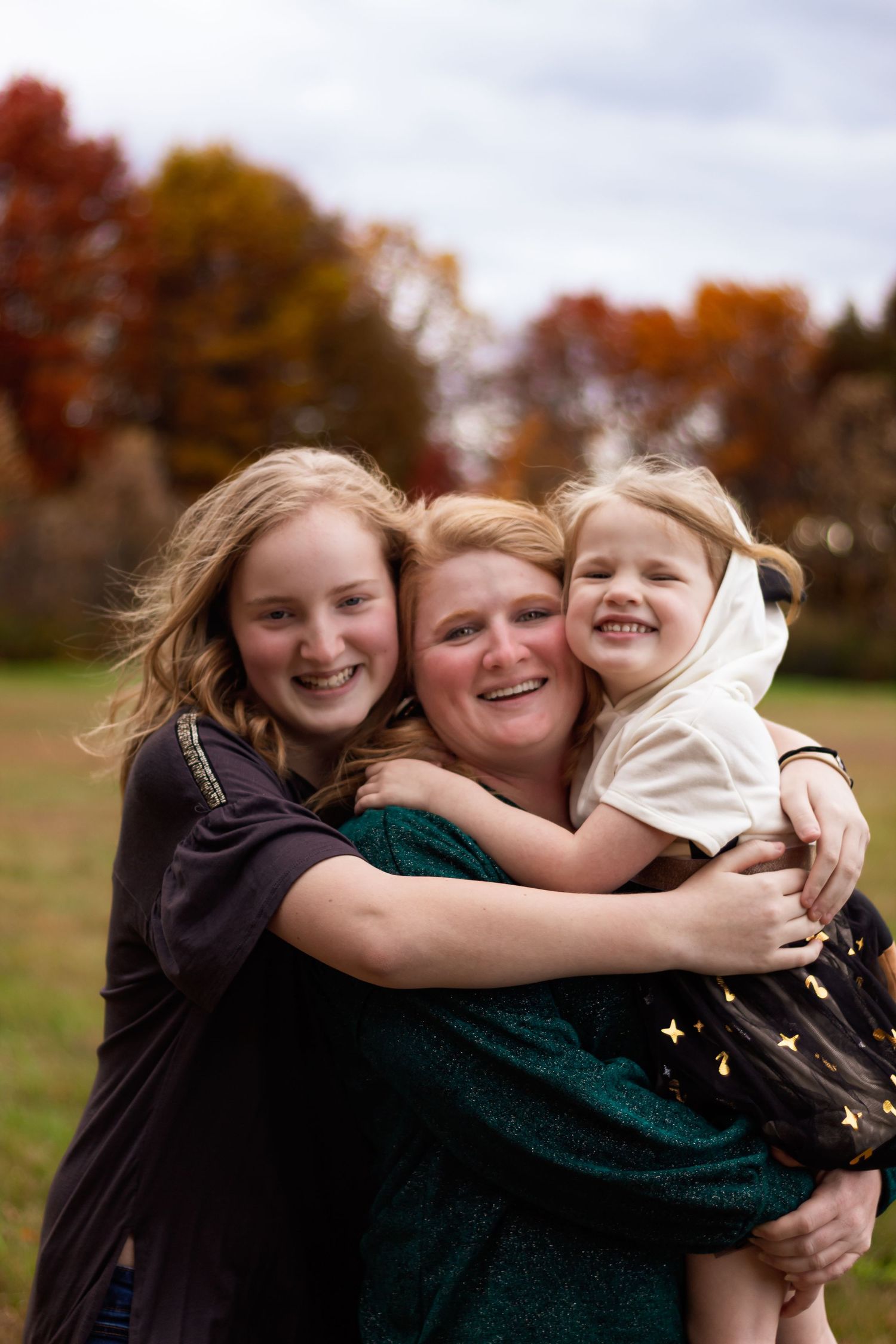 family of three, mom and two daughters standing in front of fall colors