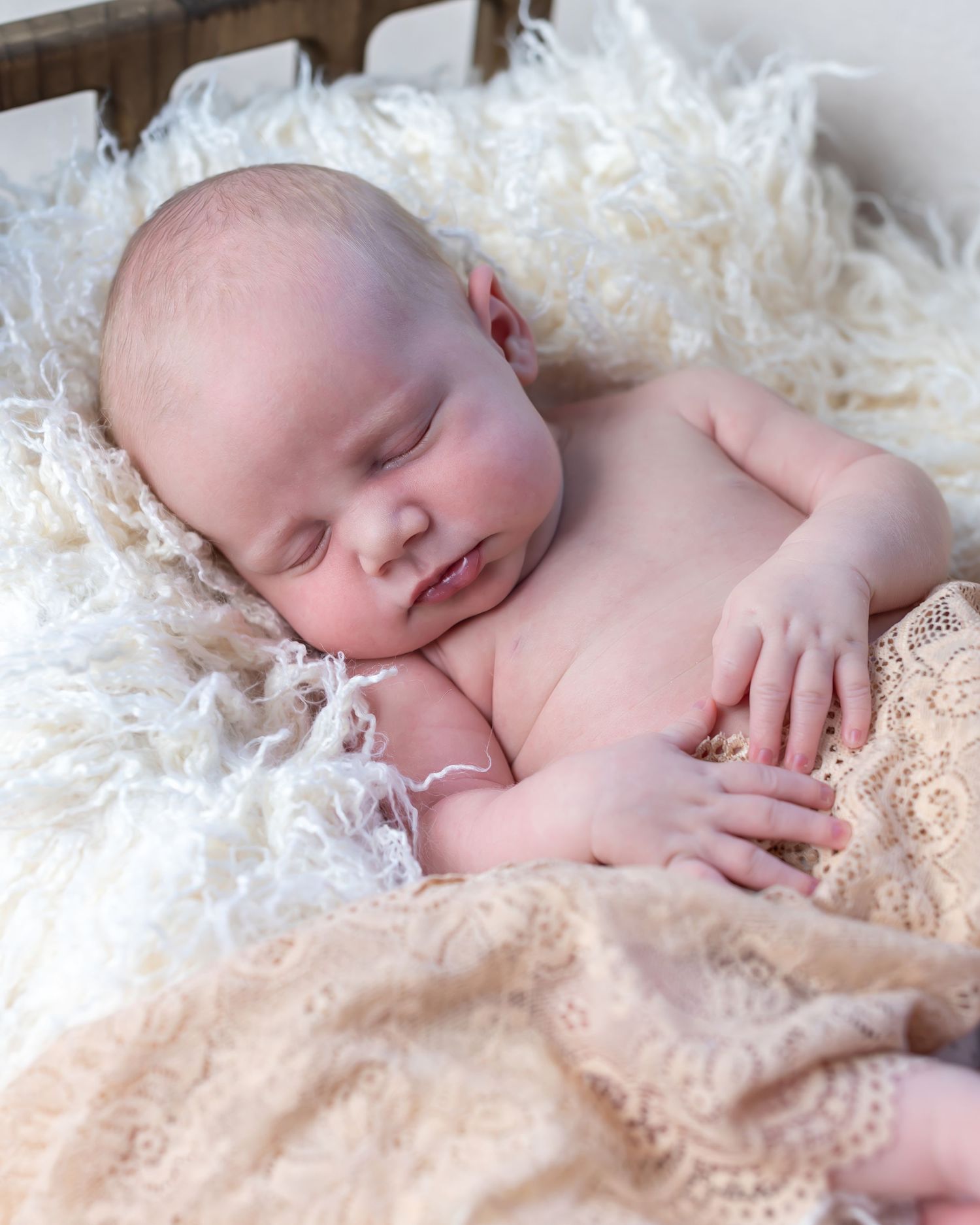 Newborn baby sleeping peacefully on soft cream lace blanket in natural light setting.