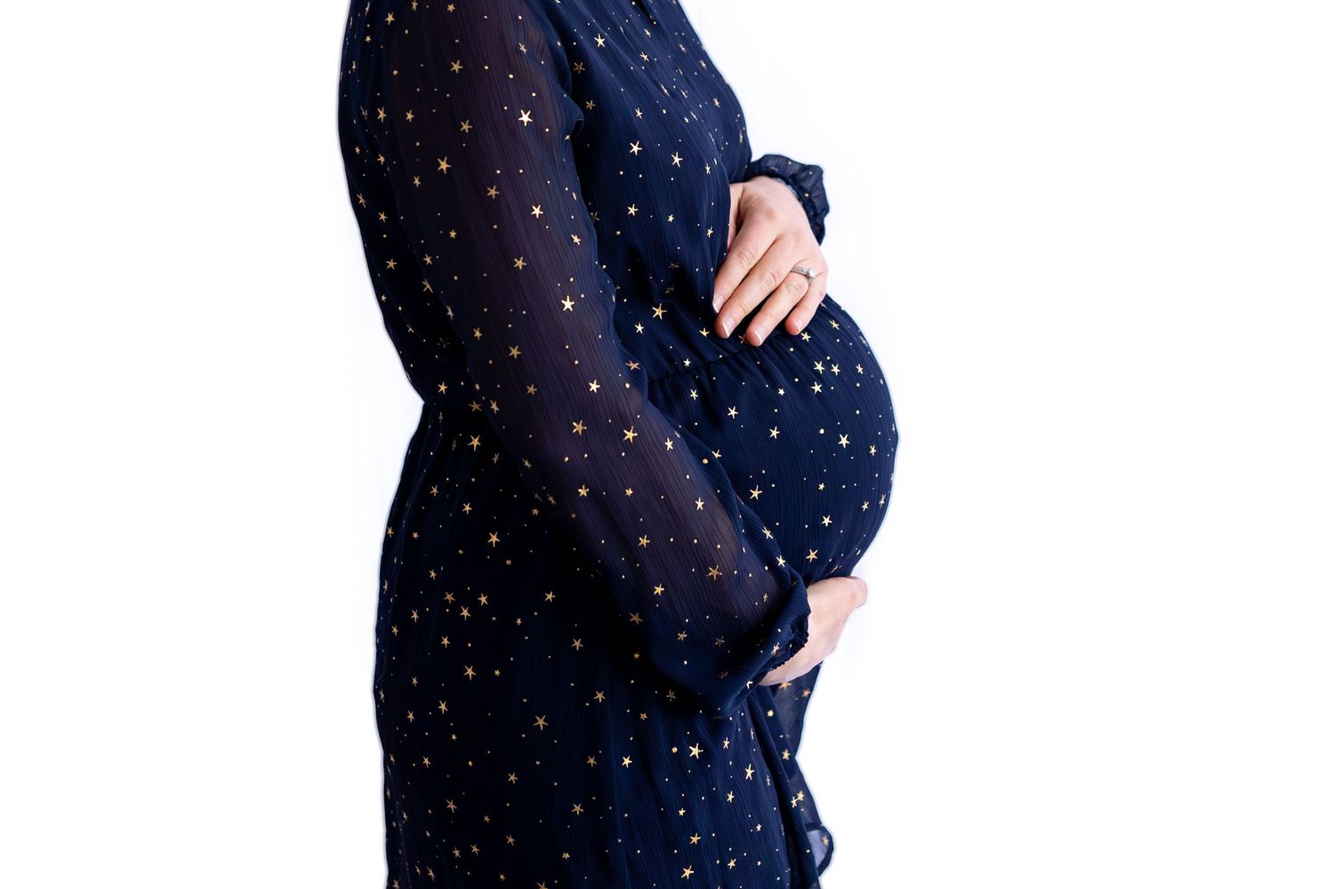 Pregnant woman in navy blue star-print dress cradling baby bump, side profile maternity photo on white background.