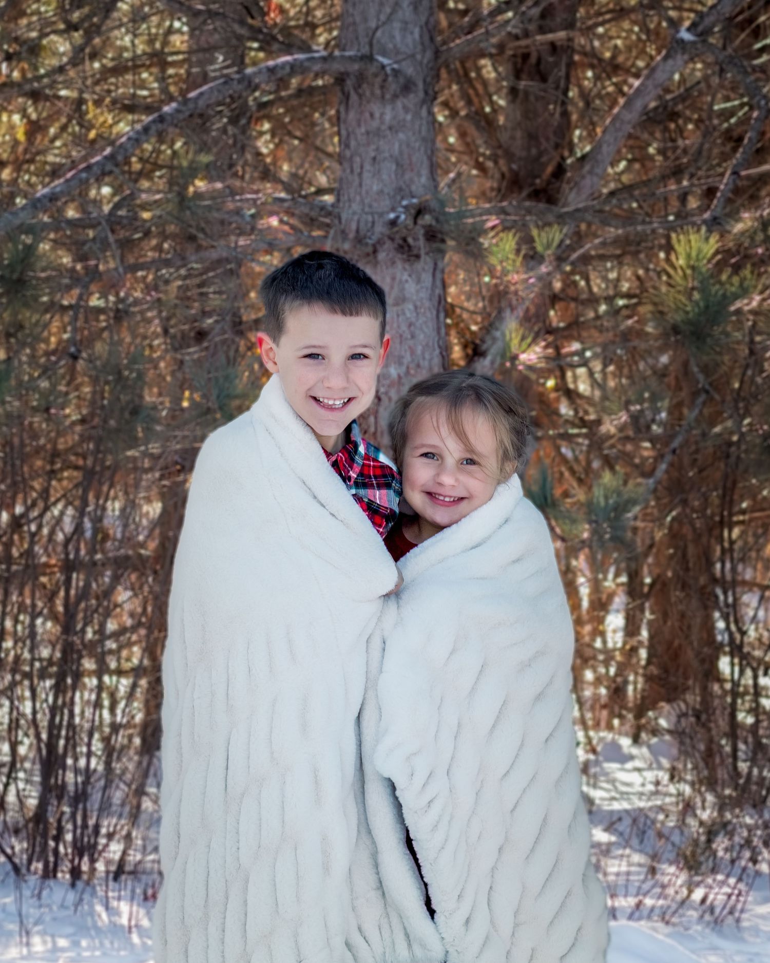 Two people wrapped in white blankets stand together in a snowy winter forest setting.